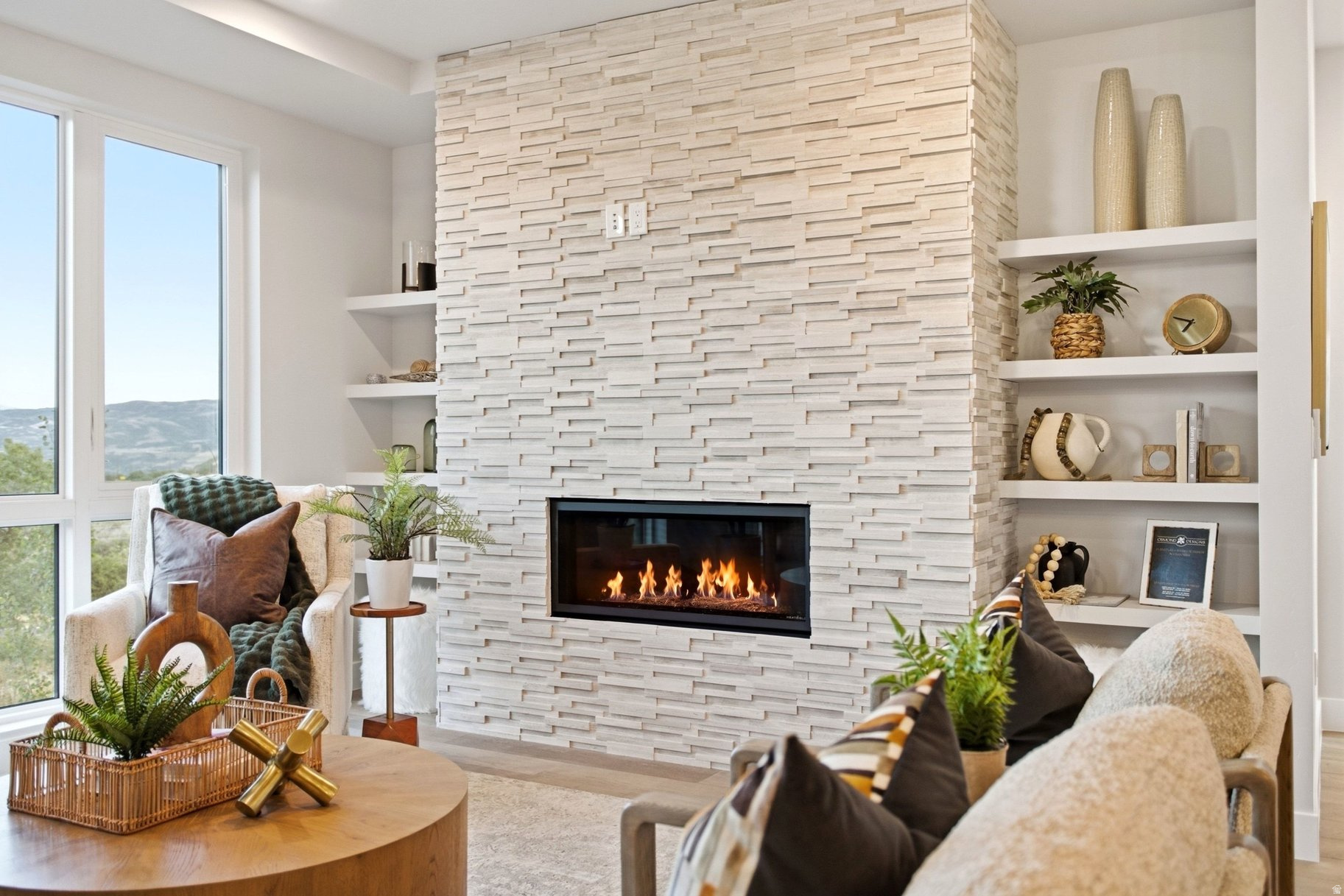 Living room with a stacked-stone fireplace, built-in shelves, and mountain views through tall windows.