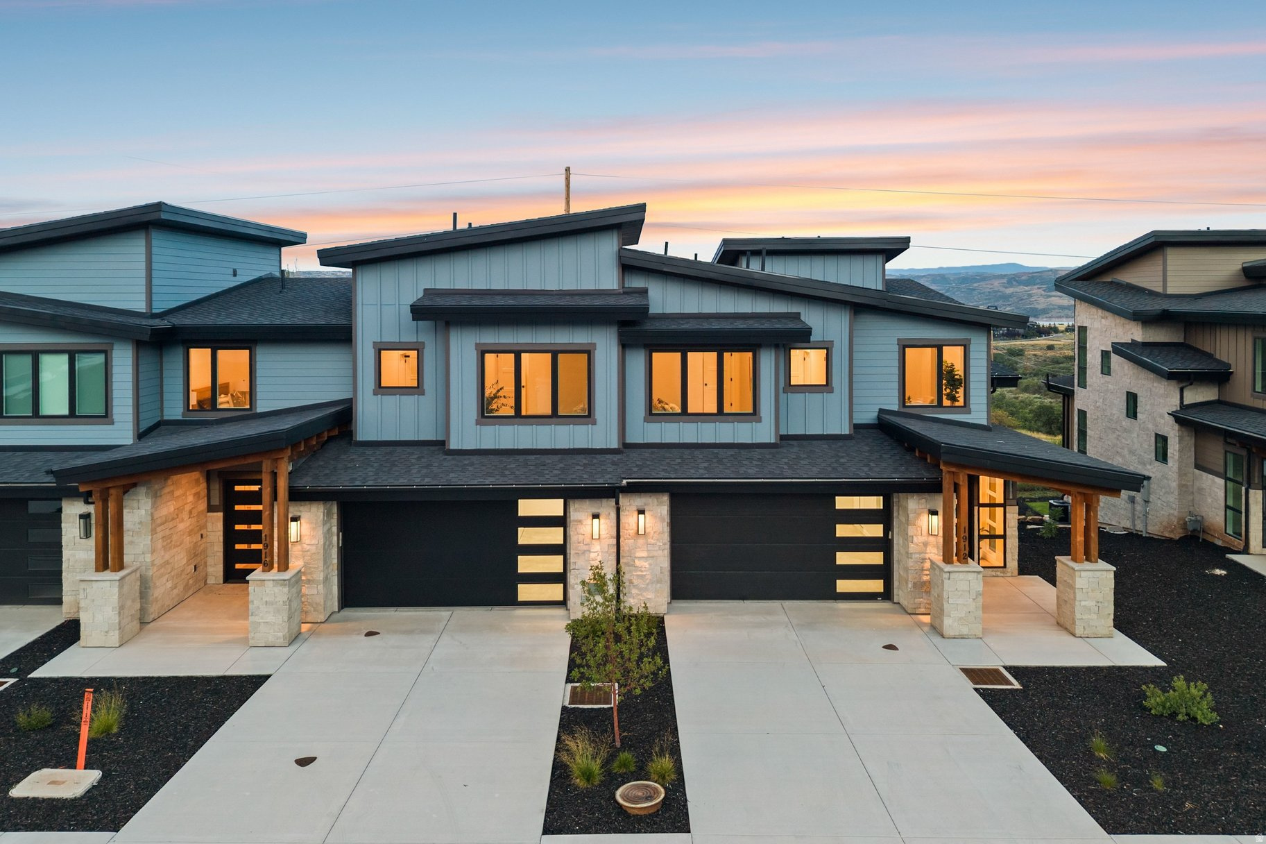 Modern blue-gray home with stone accents and glowing windows at dusk.
