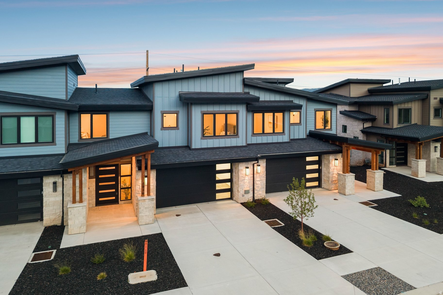 Modern attached homes with blue-gray siding and warm glowing windows at dusk.