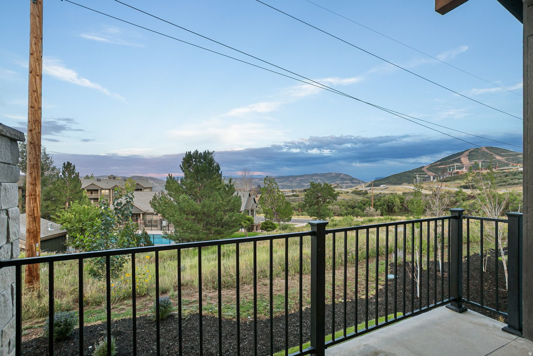 Patio overlooking neighboring homes and rolling hills beneath a partly cloudy sky.