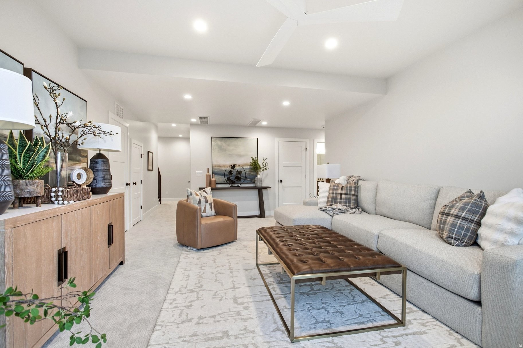 Furnished living room with a light-gray sectional, tufted coffee table, and wood sideboard.