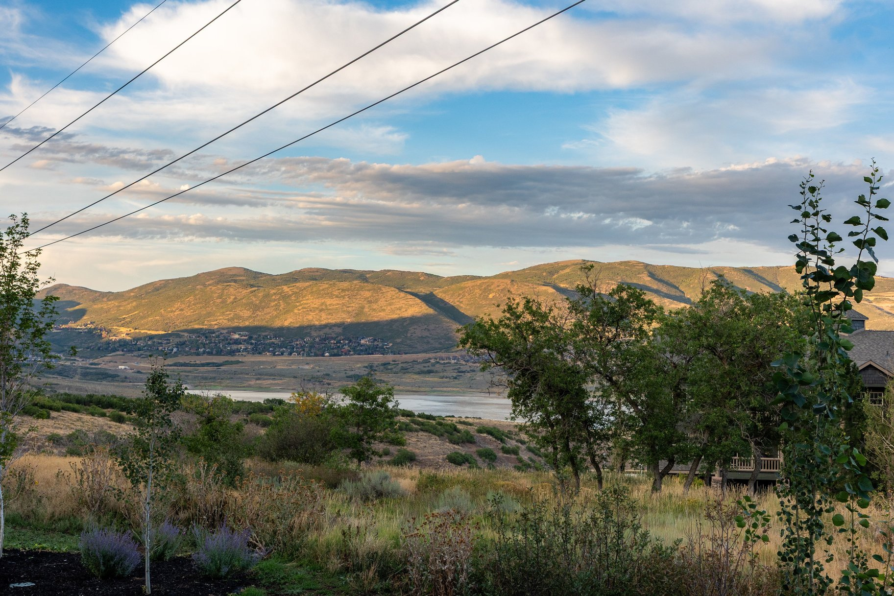 Landscaped hillside overlooking a reservoir, valley homes, and sunlit mountain ridges.