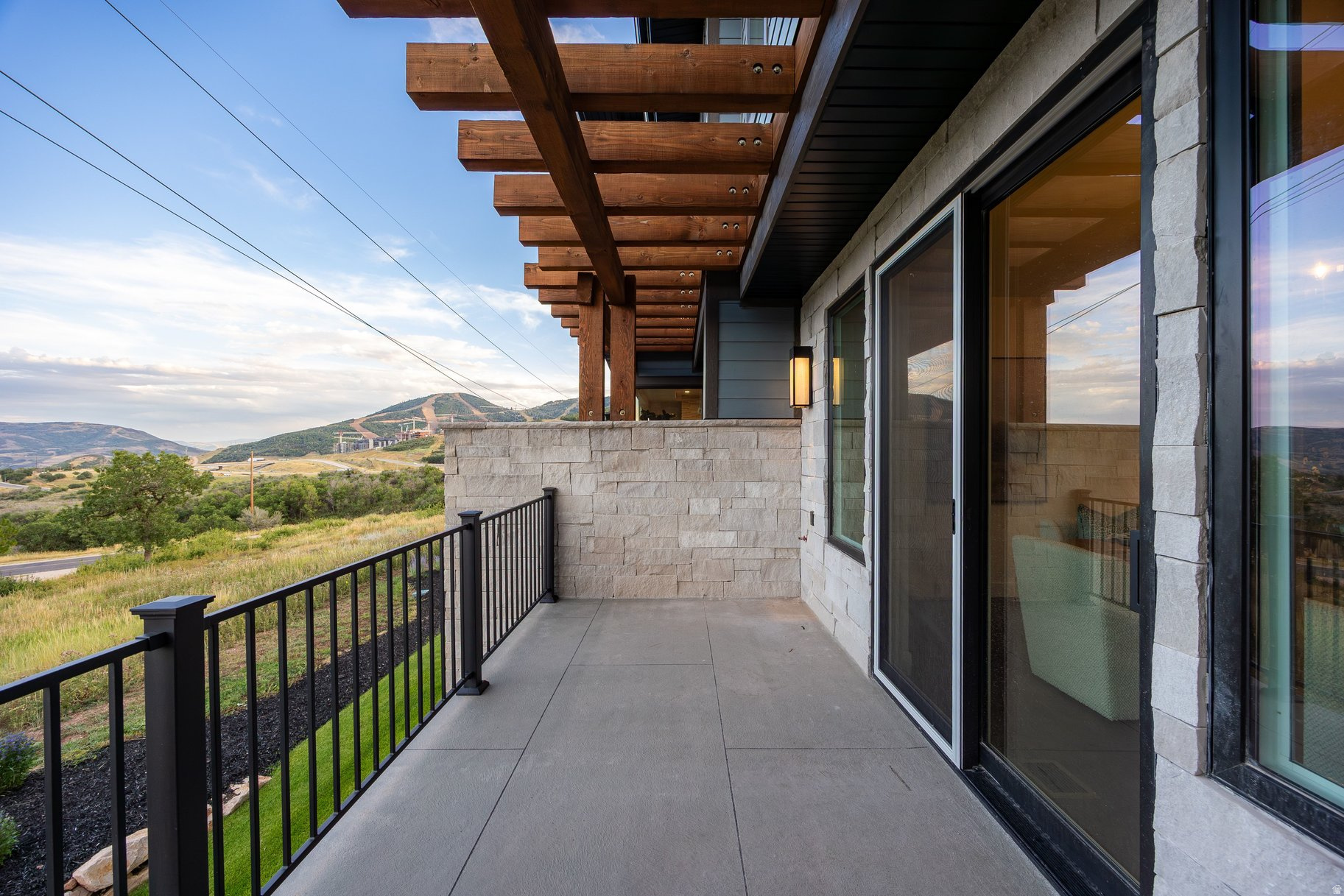Covered balcony with timber beams and stone walls overlooking a grassy hillside and mountains.