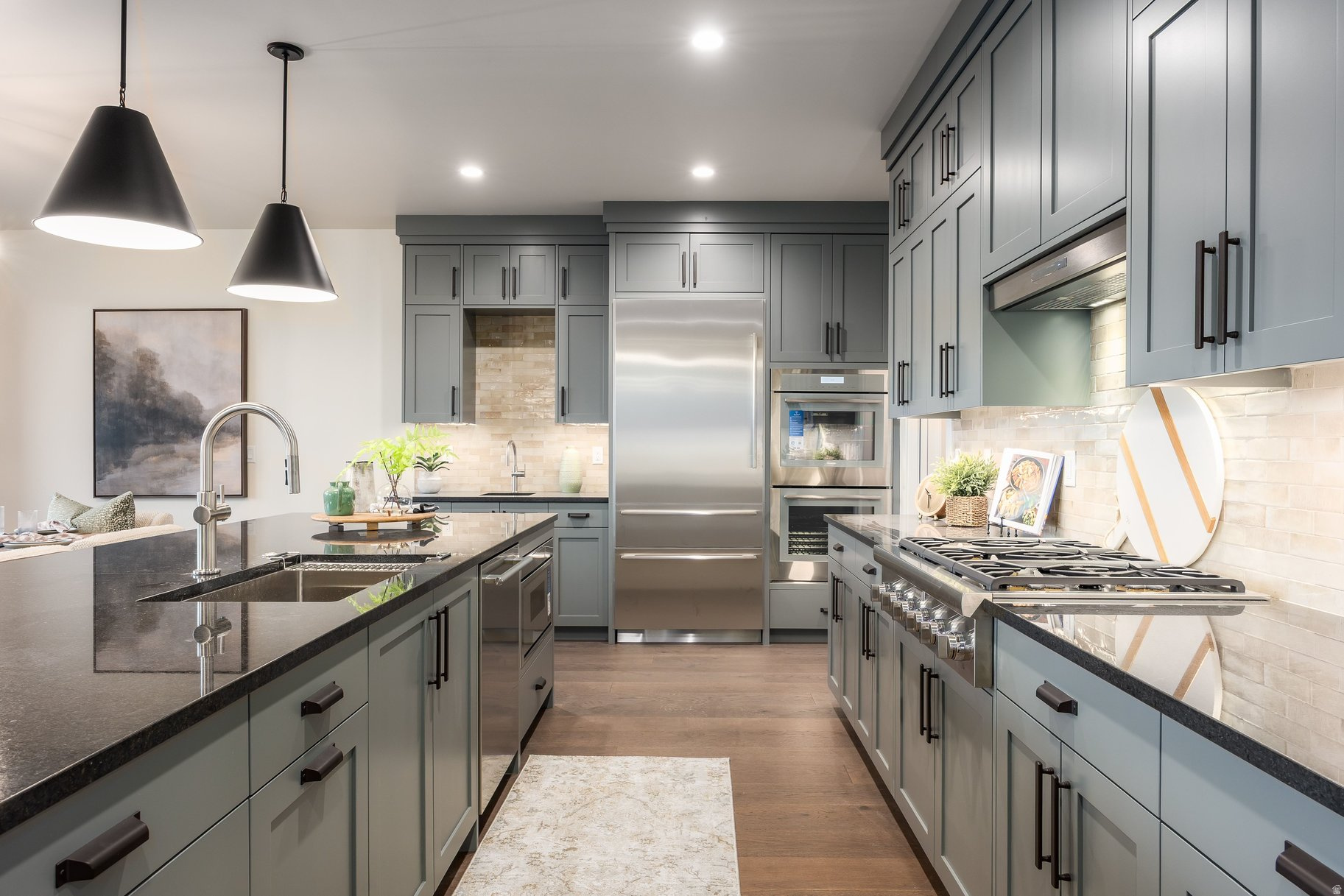 Modern kitchen with gray cabinetry, a large dark-countertop island, and stainless steel appliances.