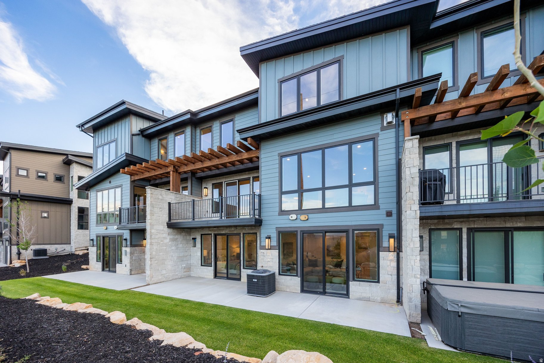 Contemporary blue-gray home with stone accents, wood pergolas, and a covered hot tub.