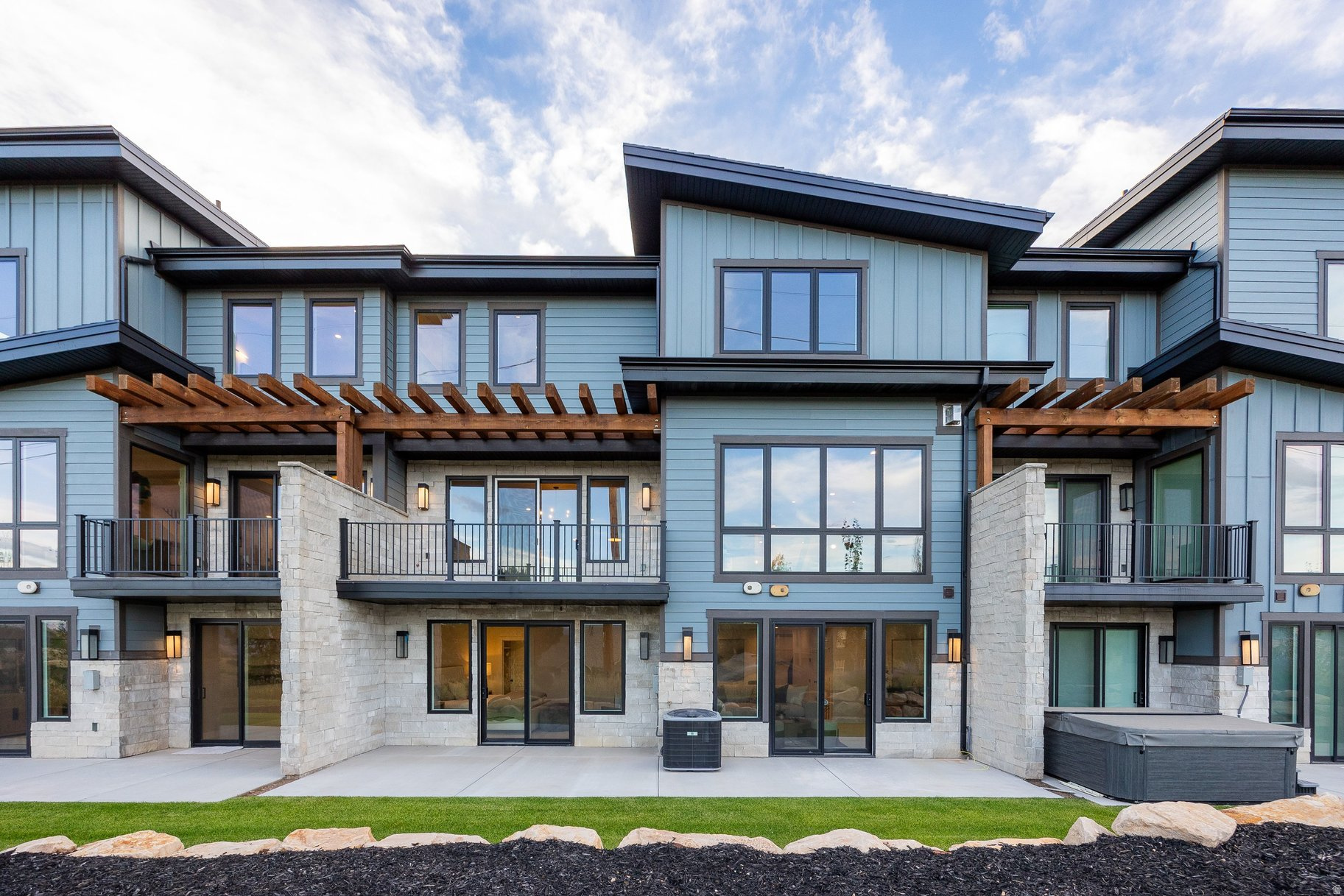 Contemporary blue-gray residence with stone walls, wood pergolas, private patios, and a covered hot tub.