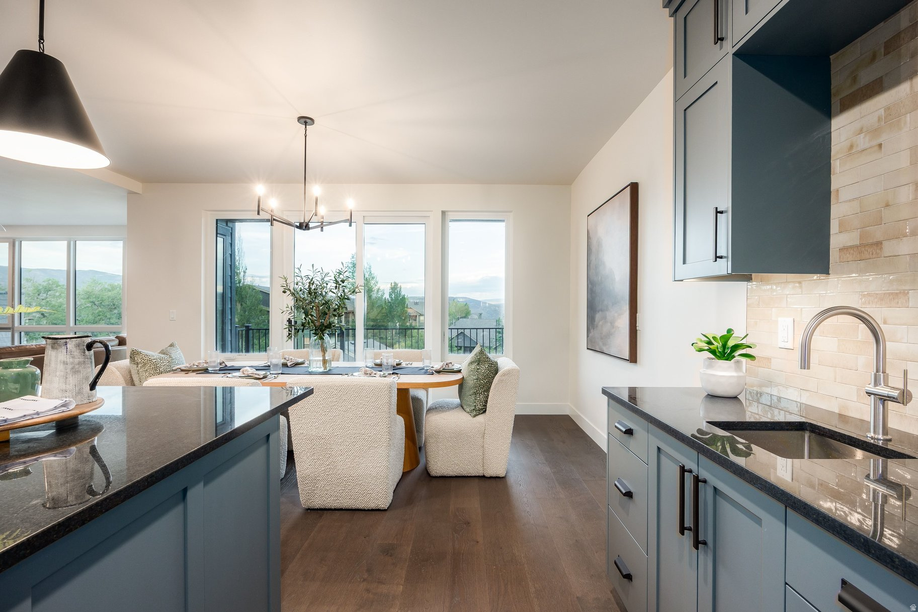 Staged kitchen and dining area with blue-gray cabinets and mountain views through large windows.