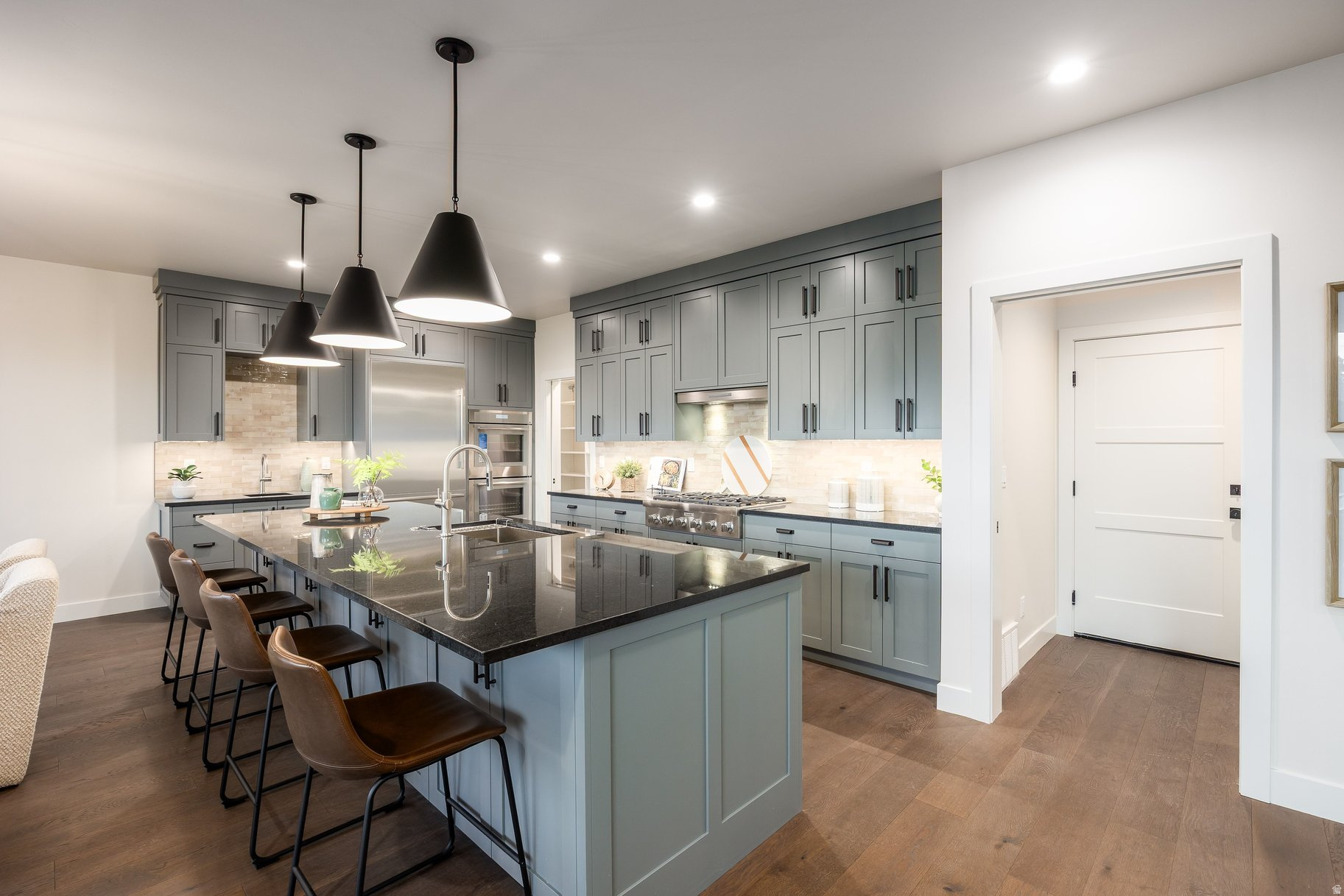 Modern kitchen with blue-gray cabinets, a large stone island, bar seating, and black pendant lights.