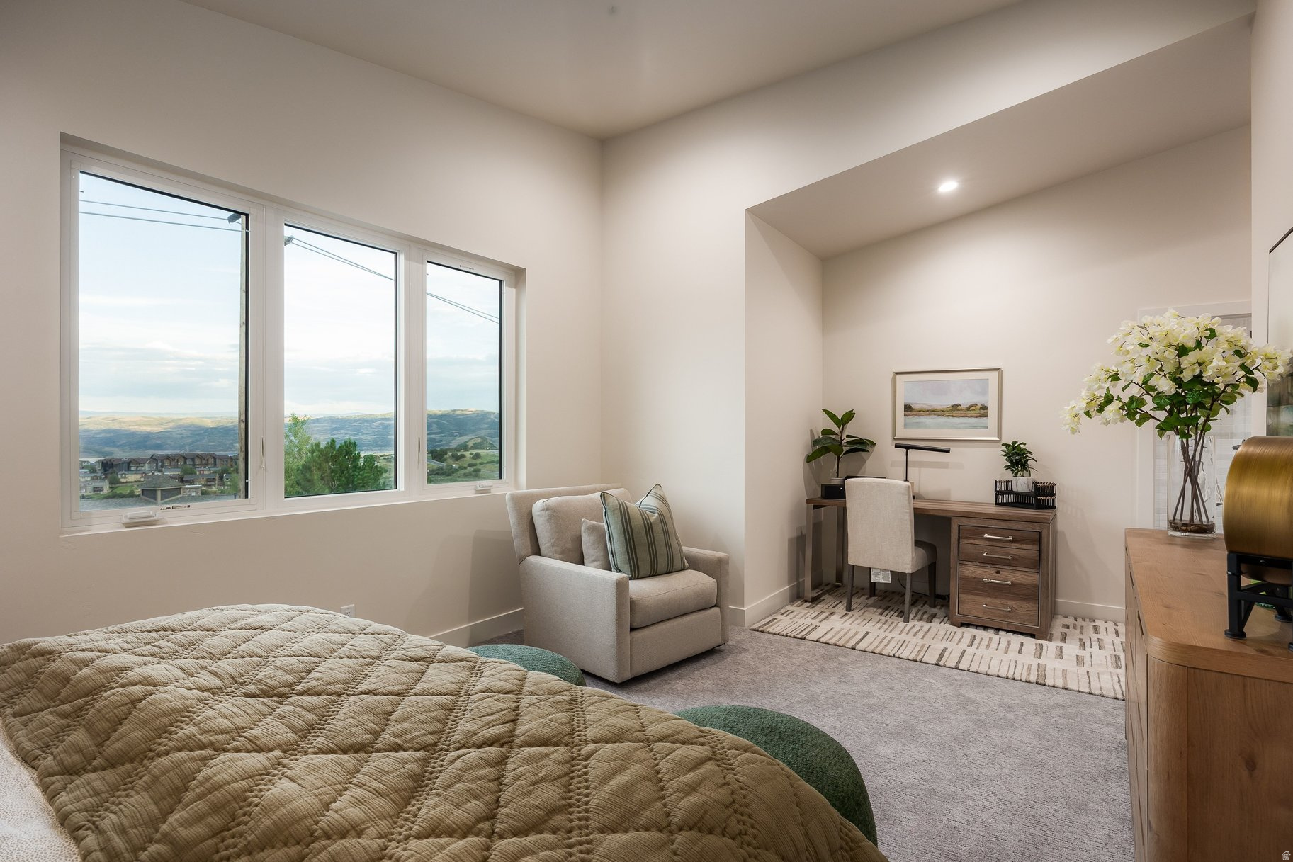 Furnished bedroom with wide windows overlooking rolling hills, a bed, and a desk alcove.