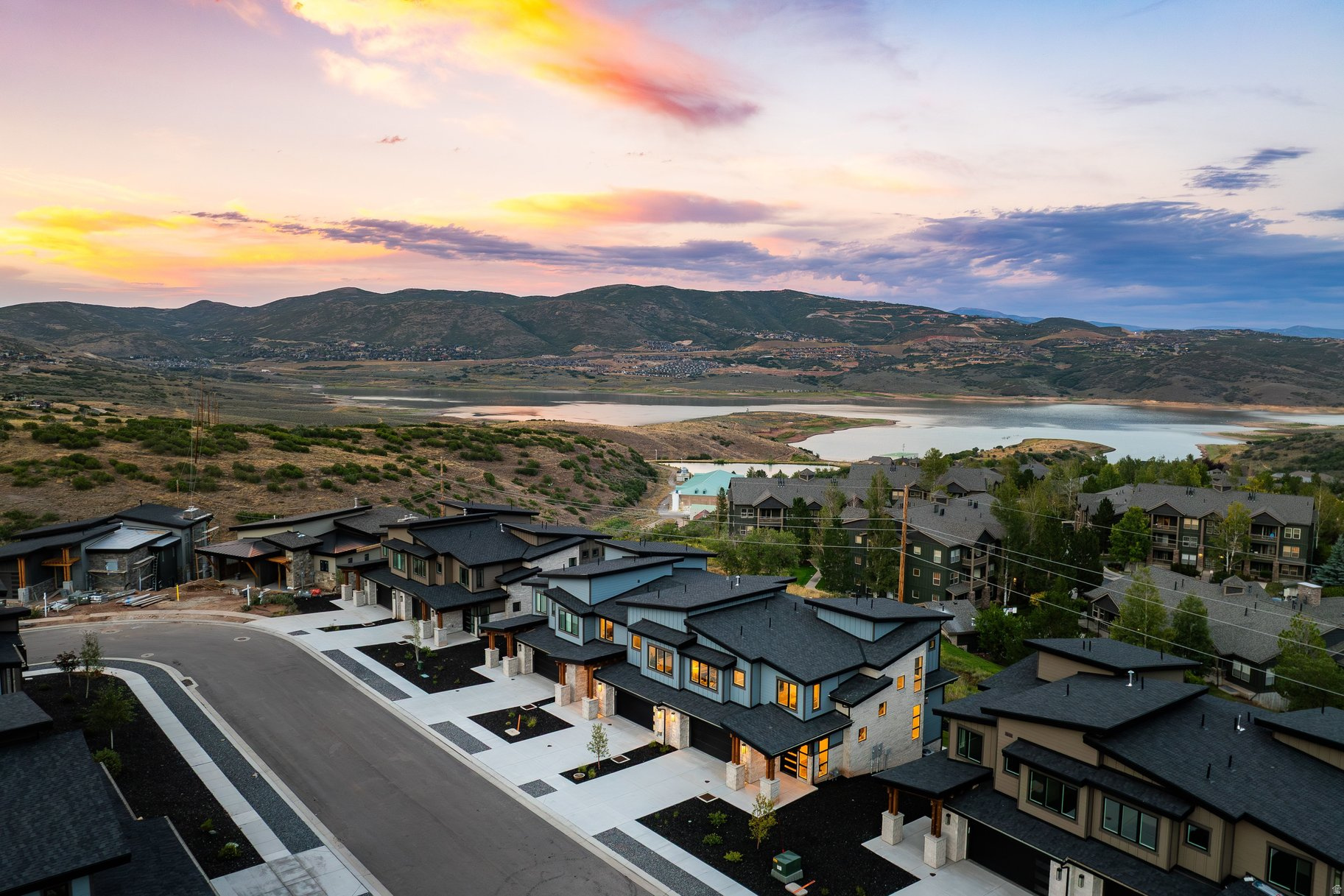 Modern homes overlook a reservoir and mountain valley beneath a colorful sunset sky.