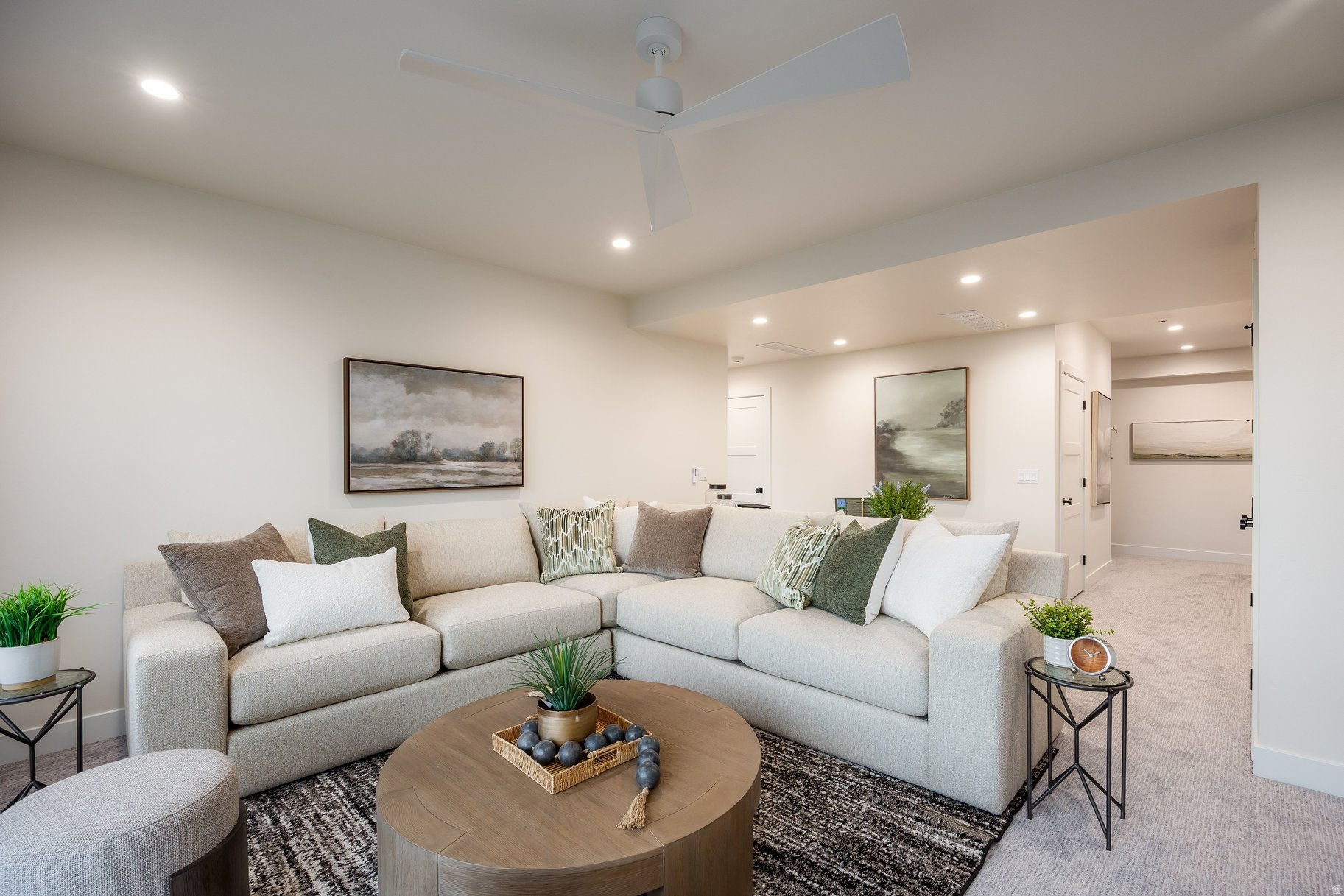 Furnished living room with a cream sectional, round wood coffee table, and white ceiling fan.