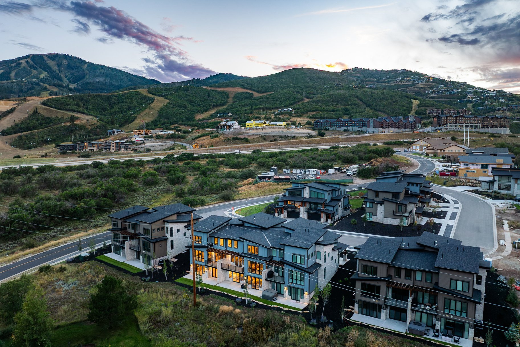 Aerial view of modern homes below green mountain hills at sunset.