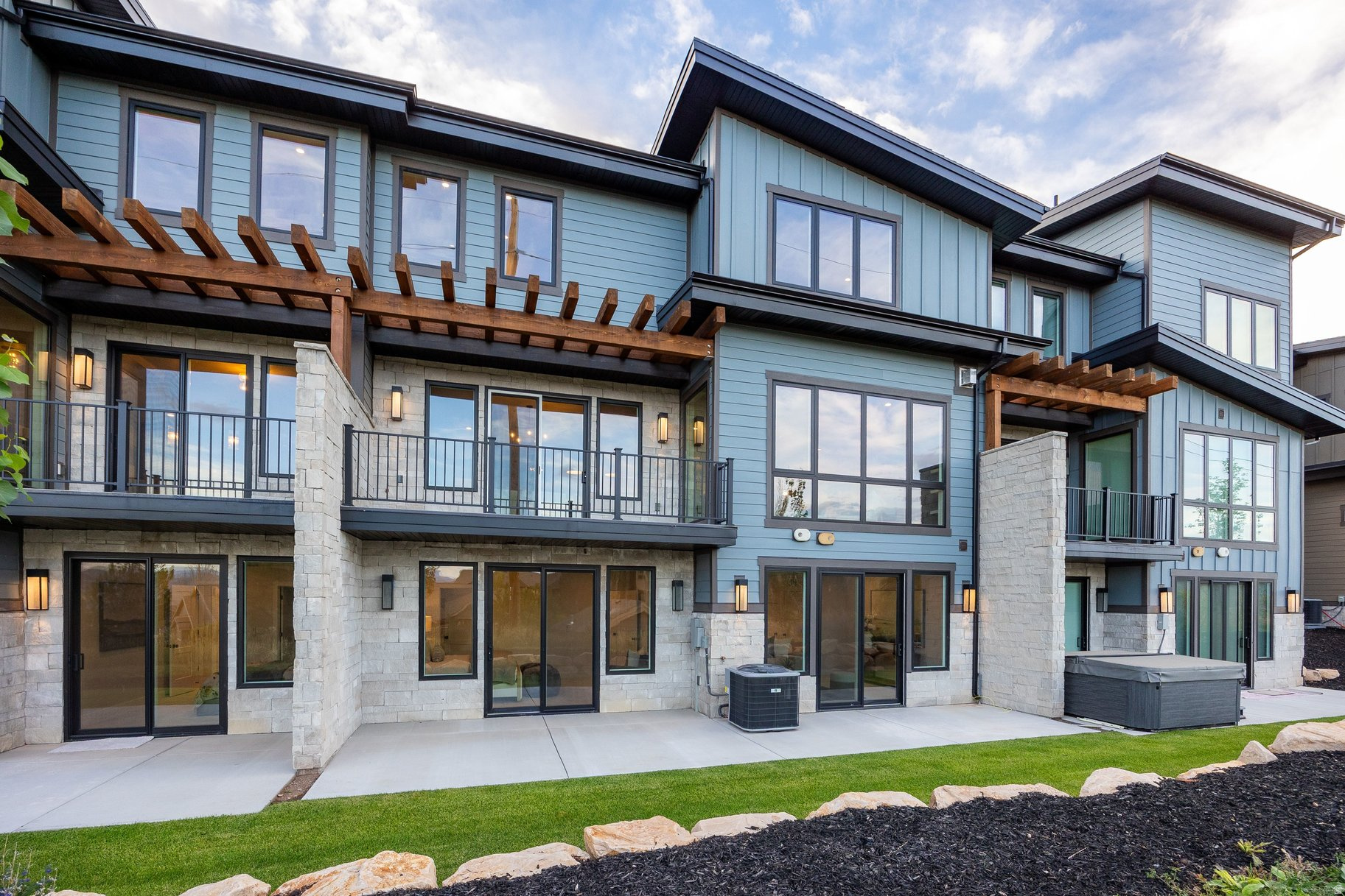 Modern blue-gray home with stone accents, wood pergolas, balconies, and a hot tub.