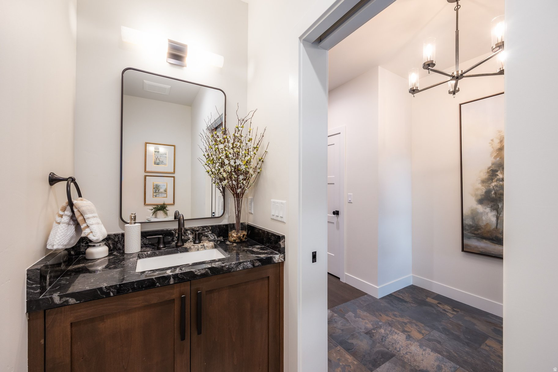 Bathroom vanity with dark marble counter and wood cabinetry beside a tiled hallway.