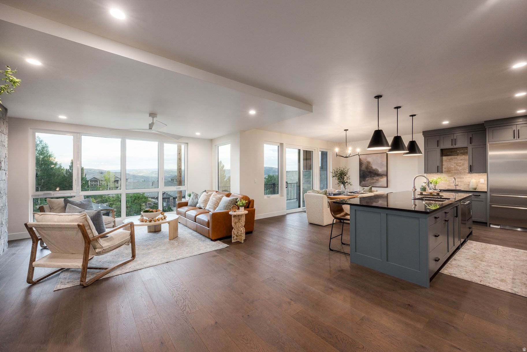 Open-plan living room and kitchen with a blue-gray island, large windows, and distant mountain views.