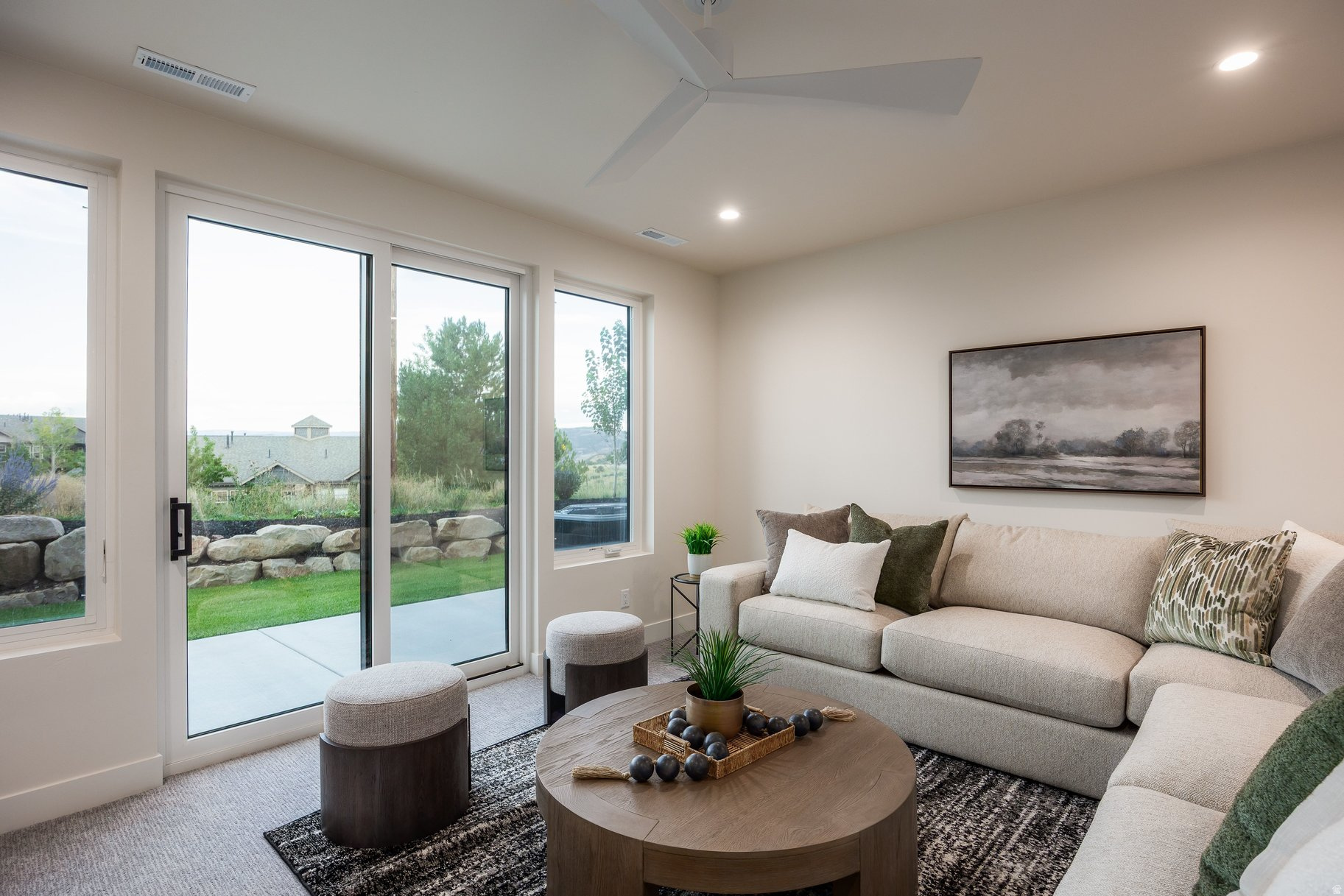 Staged living room with a light sectional sofa and sliding glass doors opening to a landscaped yard.