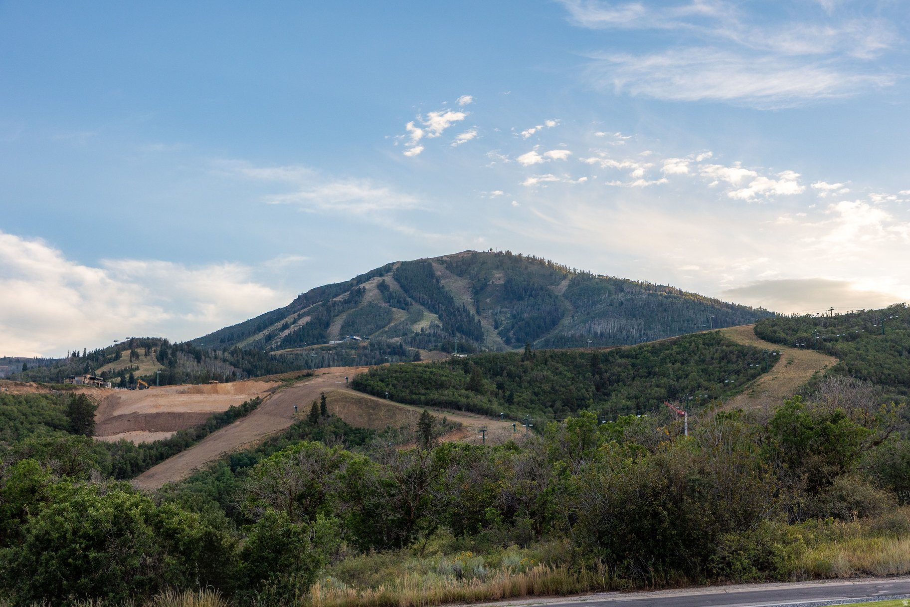 Mountain landscape with ski runs and wooded hills beyond a roadside lot.