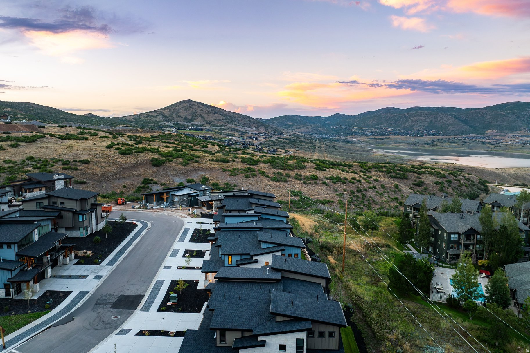 Modern homes overlook a reservoir and mountain valley beneath a pink evening sky.