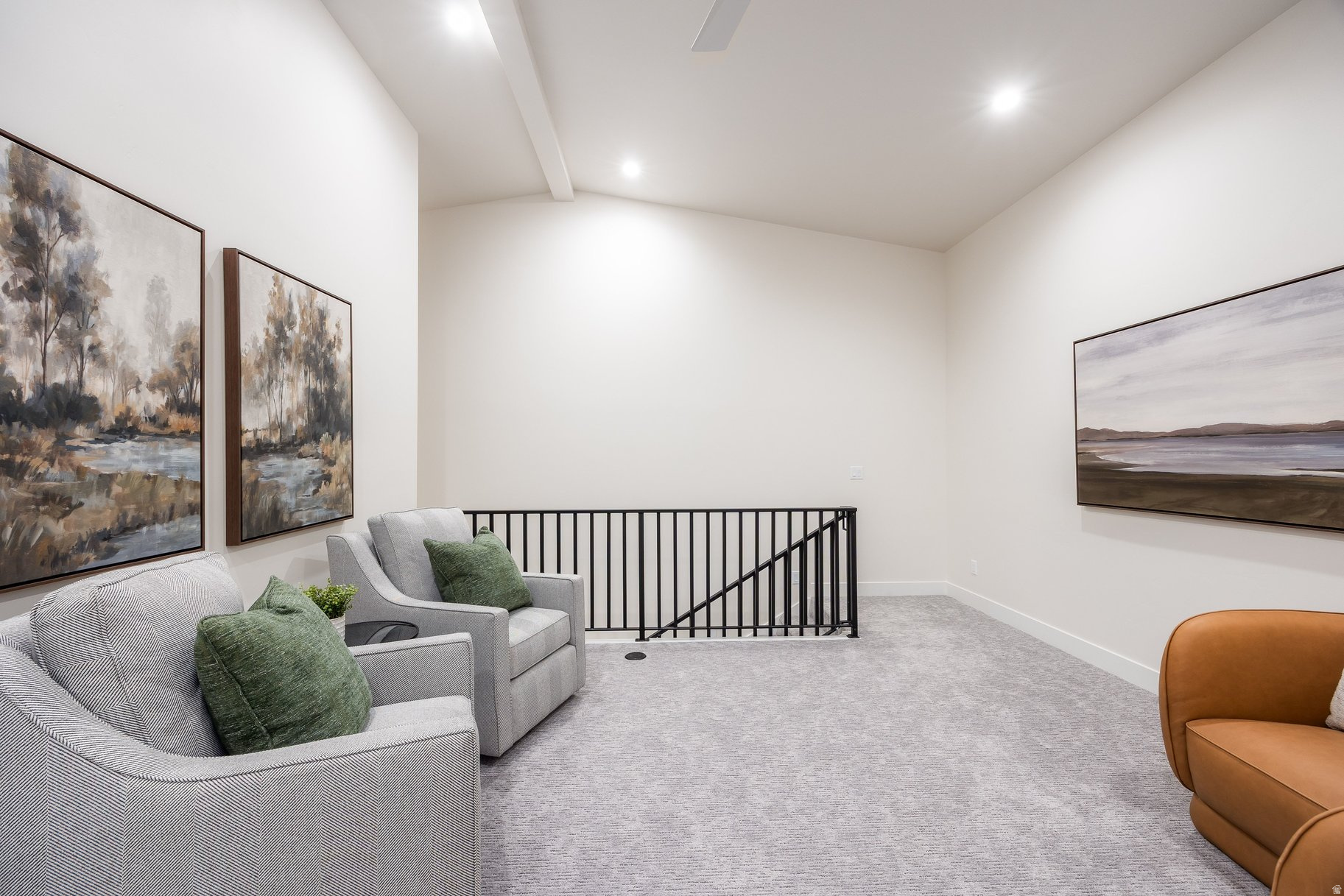 Upstairs sitting area with gray chairs, green pillows, landscape art, and a black stair railing.