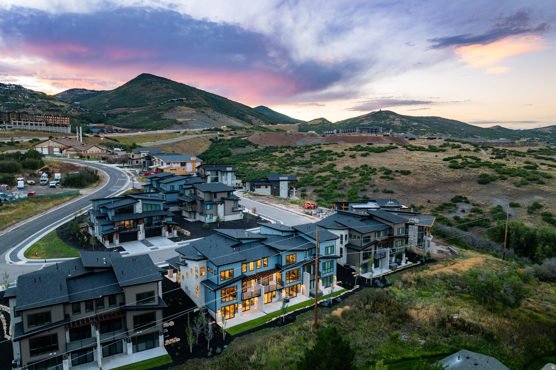 Aerial view of modern hillside homes with mountain ridges beneath a colorful sunset sky.