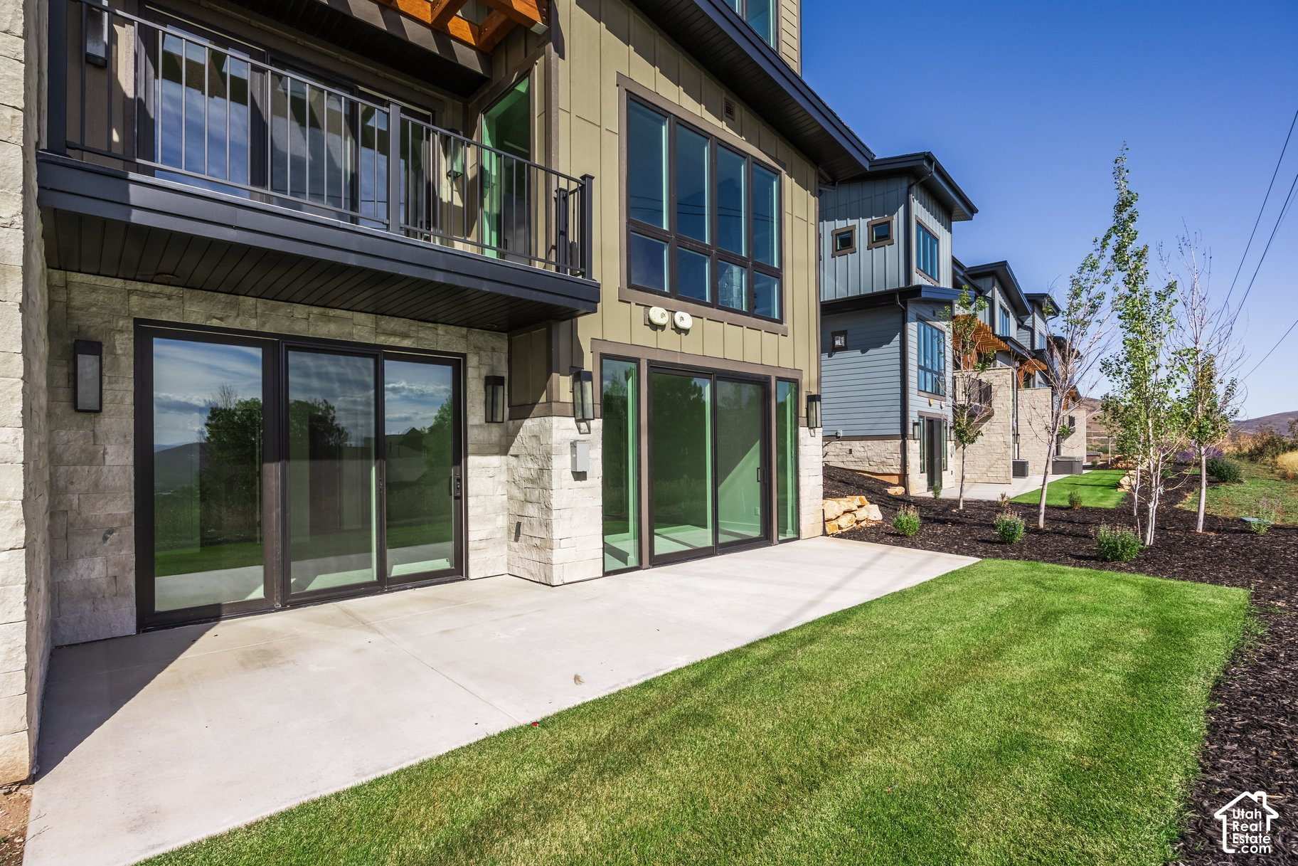 Modern townhome exterior with stonework, a balcony, sliding glass doors, and a lawn-side patio.