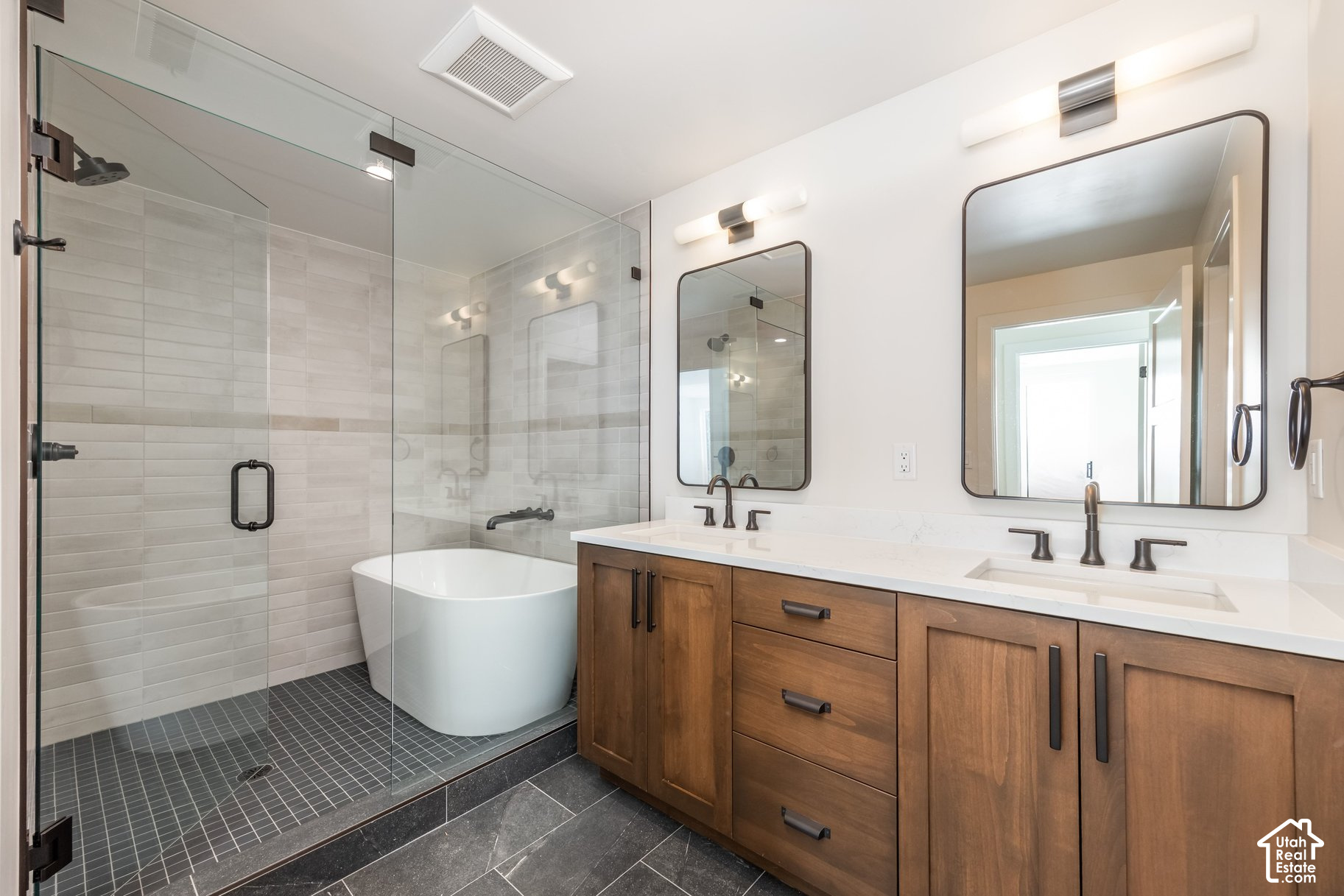 Modern bathroom with a glass walk-in shower, freestanding tub, and double-sink wood vanity.