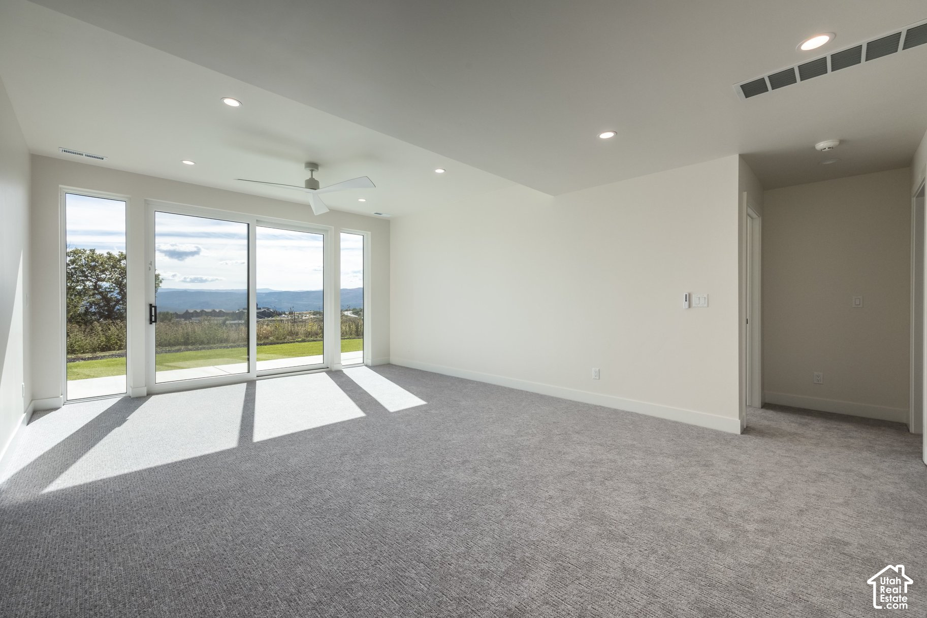 Empty living room with large glass doors, gray carpet, and distant mountain views.