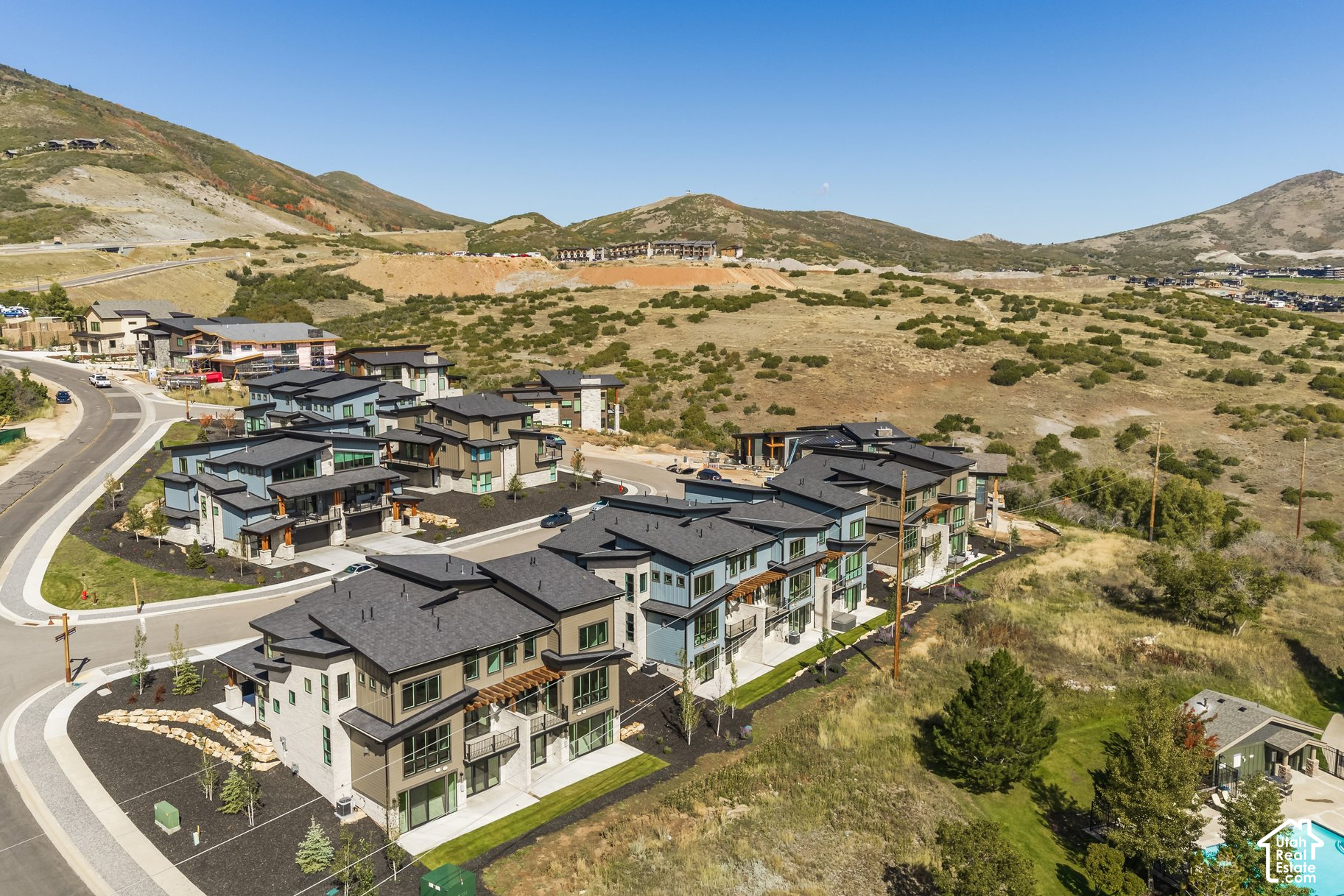 Aerial view of modern townhomes along a winding road, with rolling mountain hills beyond.