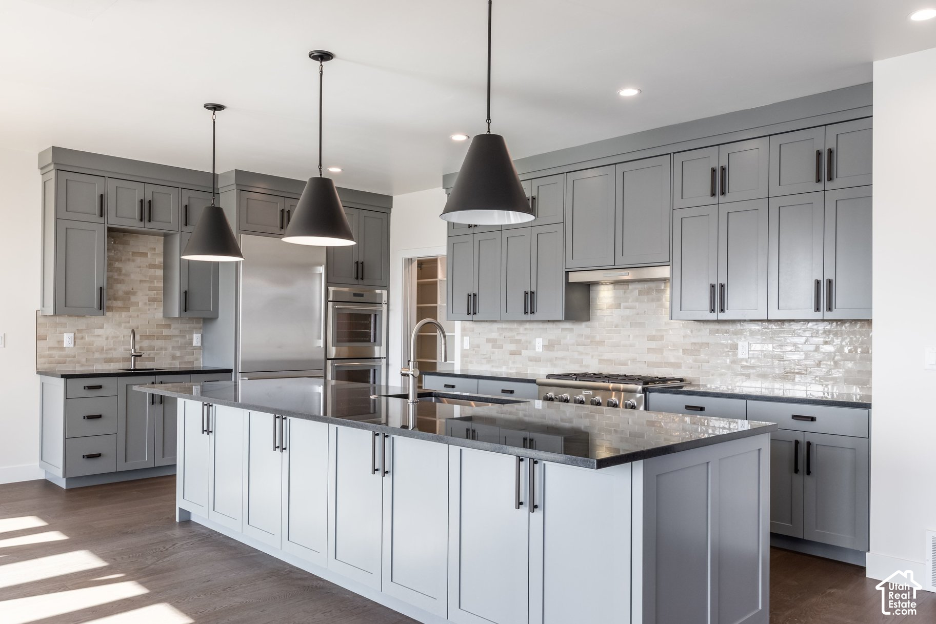 Modern kitchen with gray cabinetry, a large island, black pendant lights, and stainless steel appliances.