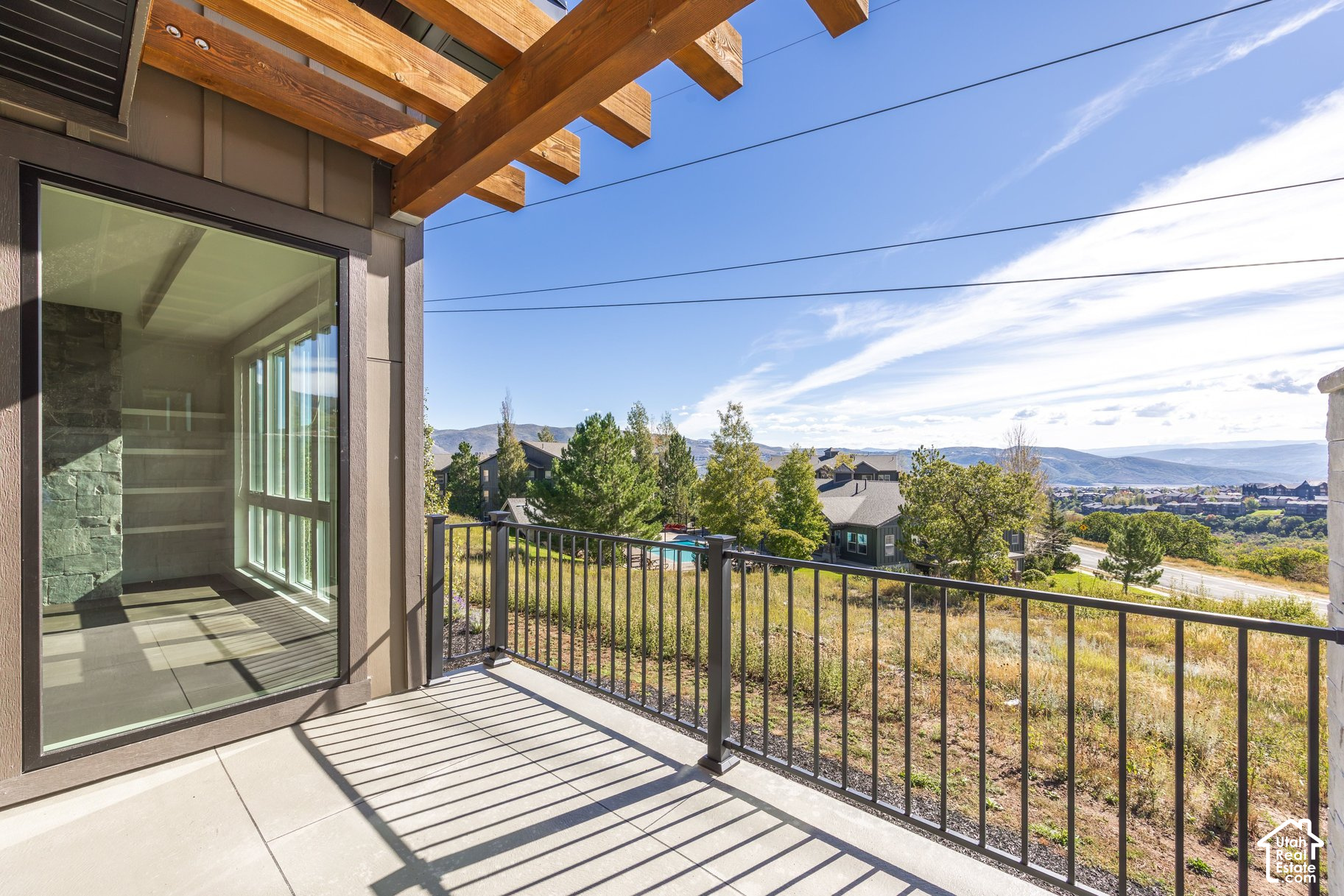 Covered balcony with timber pergola, black railing, and views of mountains and nearby homes.