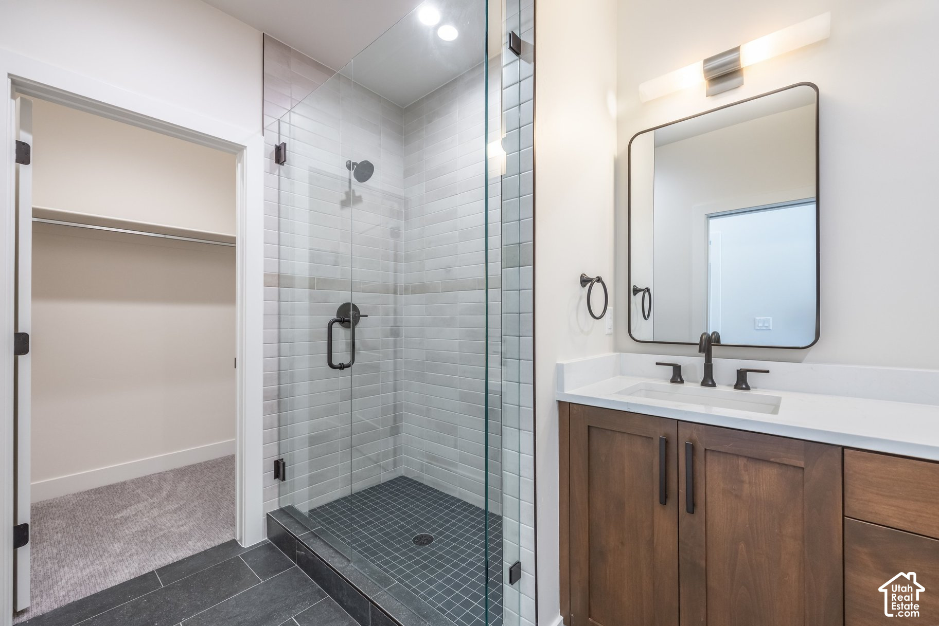 Bathroom with glass walk-in shower, wood vanity, and an open closet beside it.
