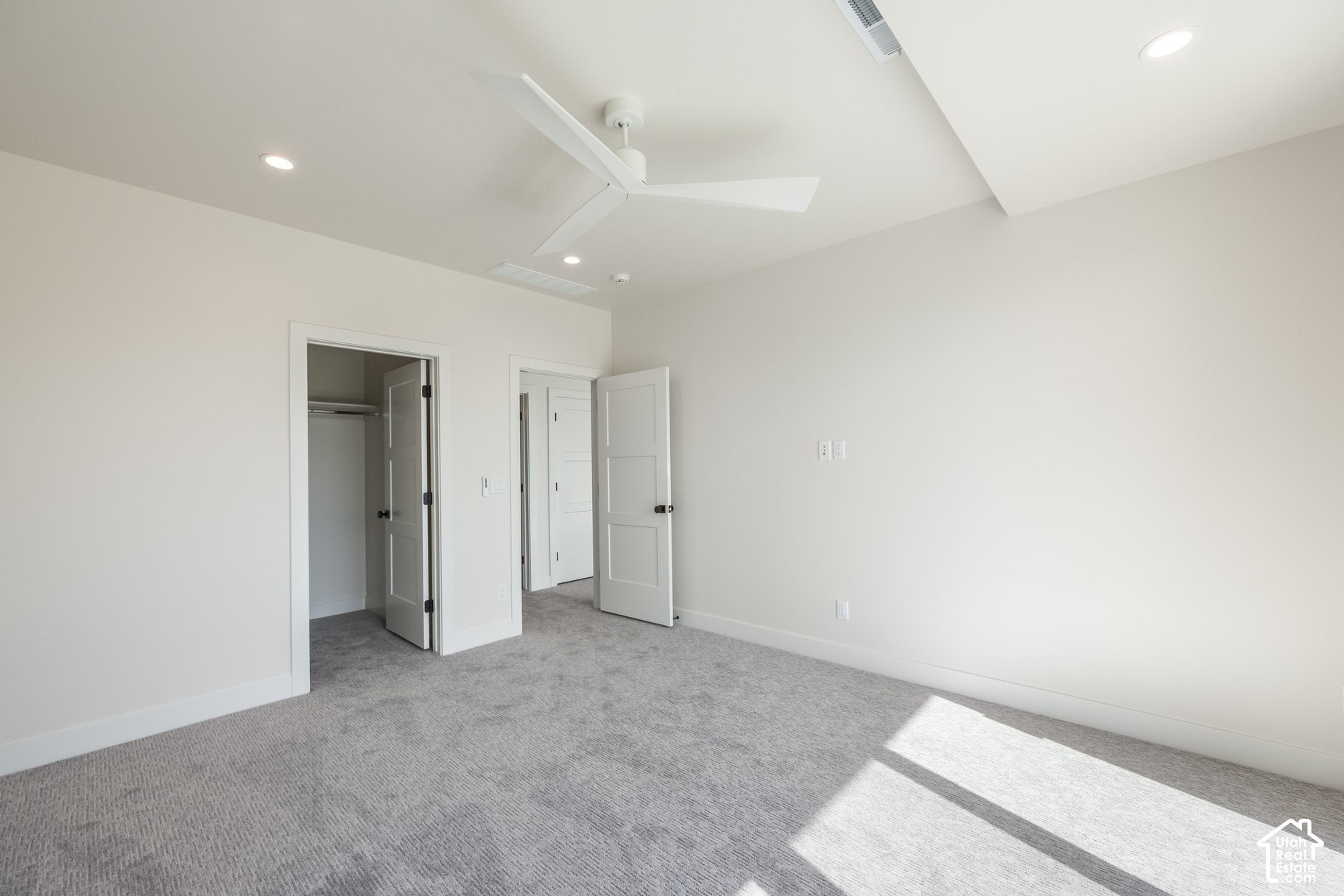 Empty bedroom with gray carpet, a white ceiling fan, and an open closet.