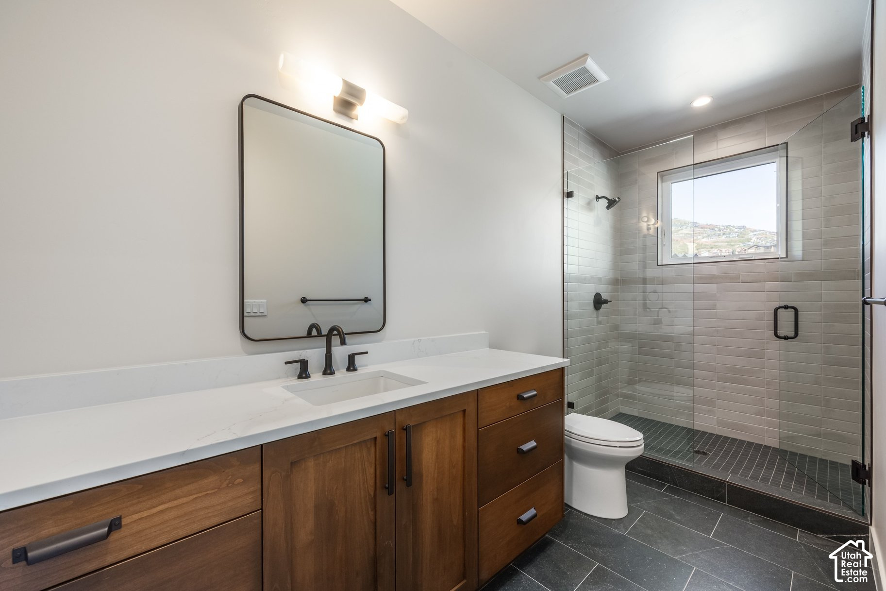 Modern bathroom with a wood vanity and glass-enclosed tiled shower with a window.