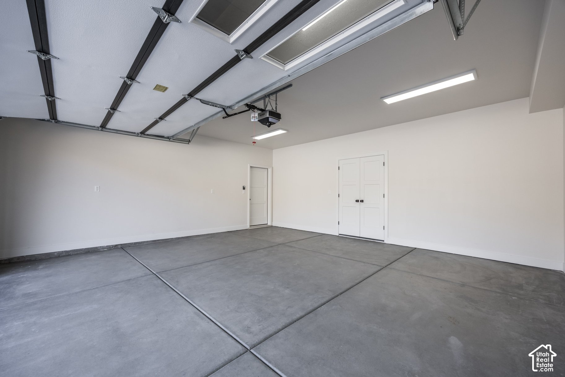Empty garage with a concrete floor, open overhead door, and double storage doors.