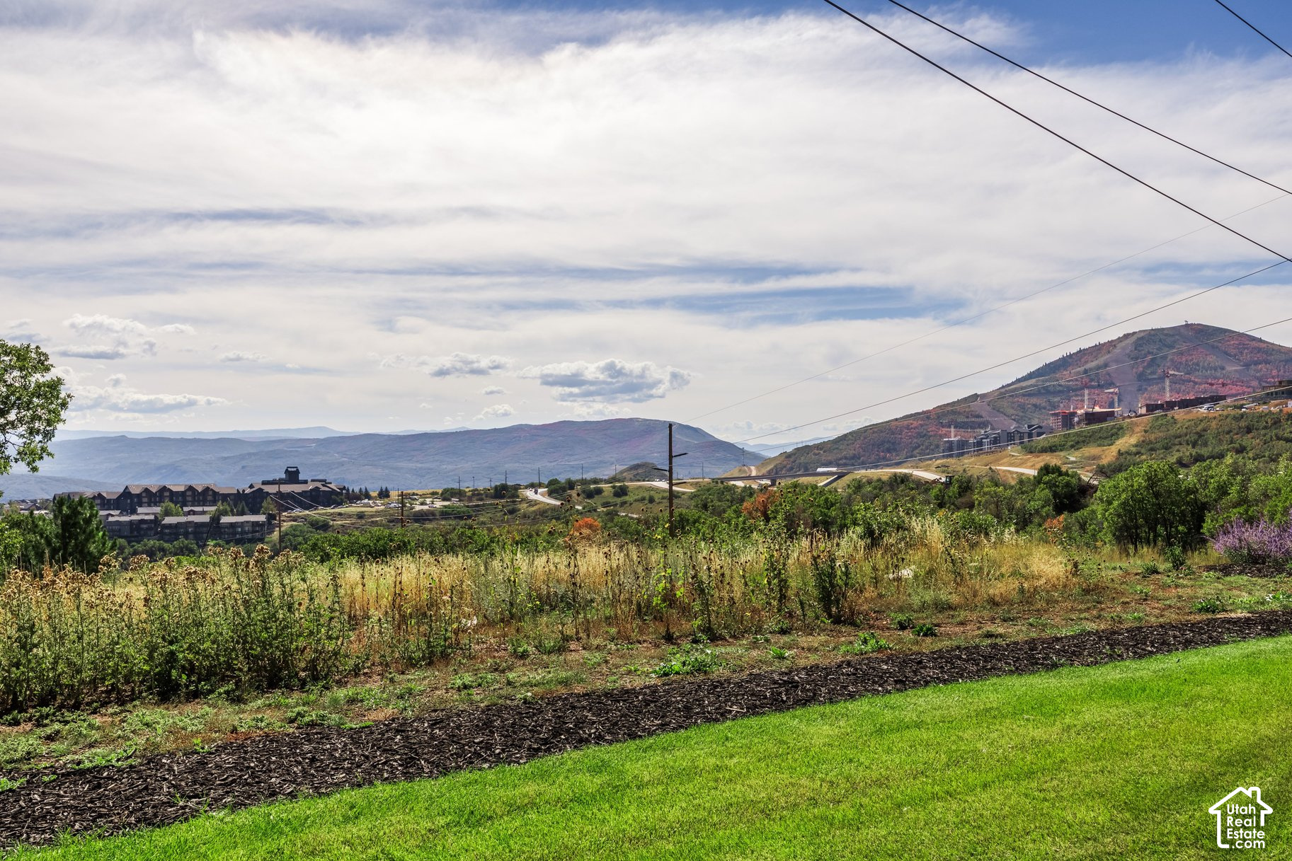 Mountain valley view from landscaped grounds, with hillside buildings and utility lines crossing the sky.