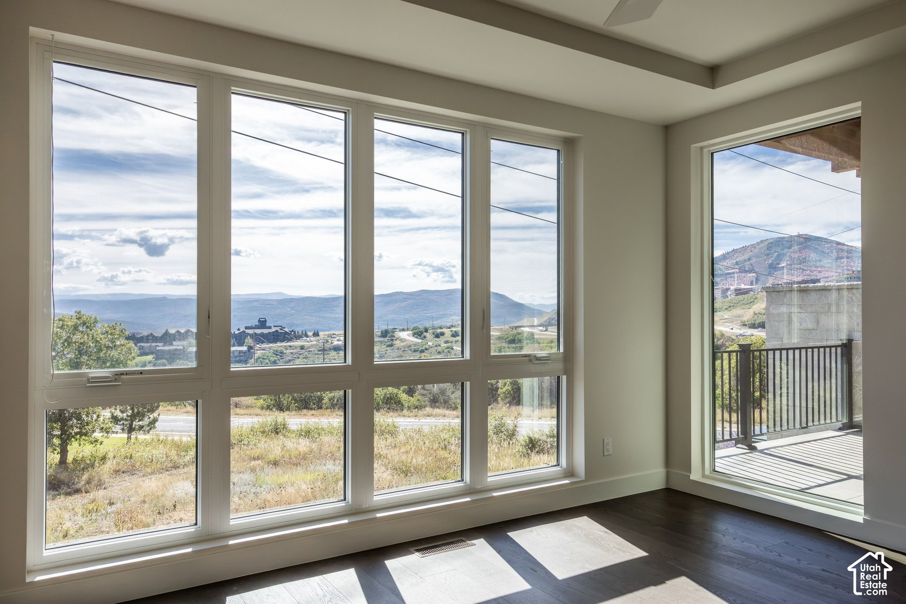 Unfurnished room with large windows overlooking mountains and a glass door to a balcony.