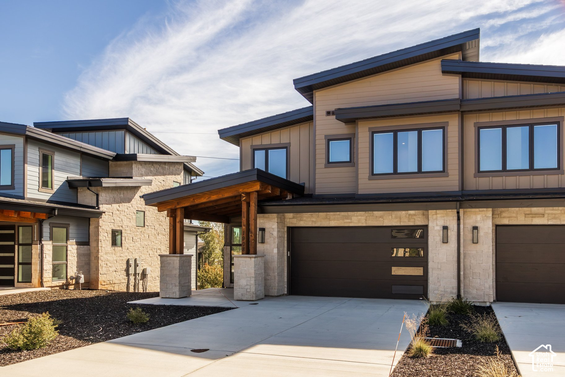Modern two-story home with stone façade, covered timber entry, and wide driveway.