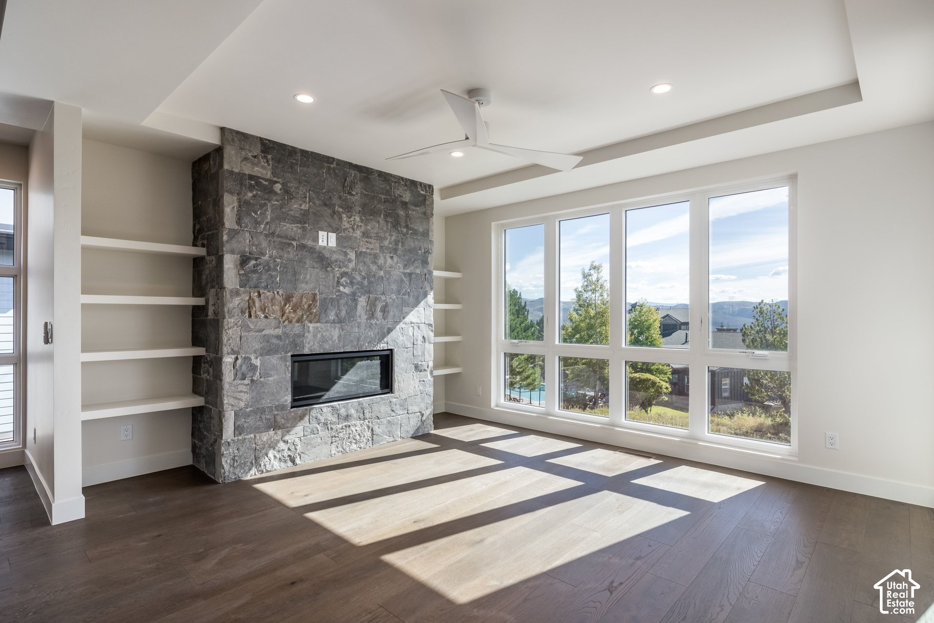 Living room with a gray stone fireplace, built-in shelving, and wide windows overlooking mountains.