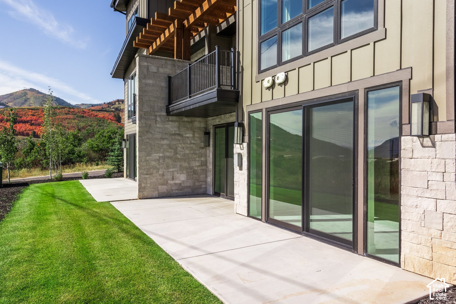 Modern mountain home with stone accents, a covered balcony, and patio overlooking autumn-colored hills.