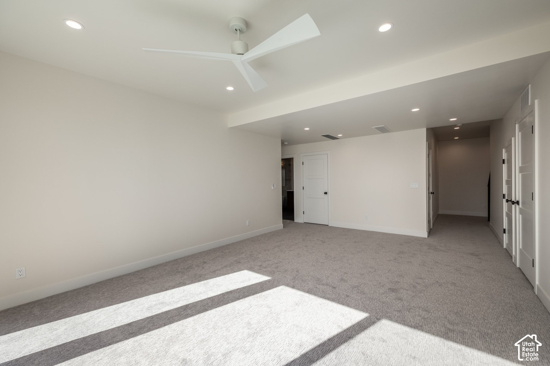 Empty carpeted bedroom with a white ceiling fan and sunlight across the floor.