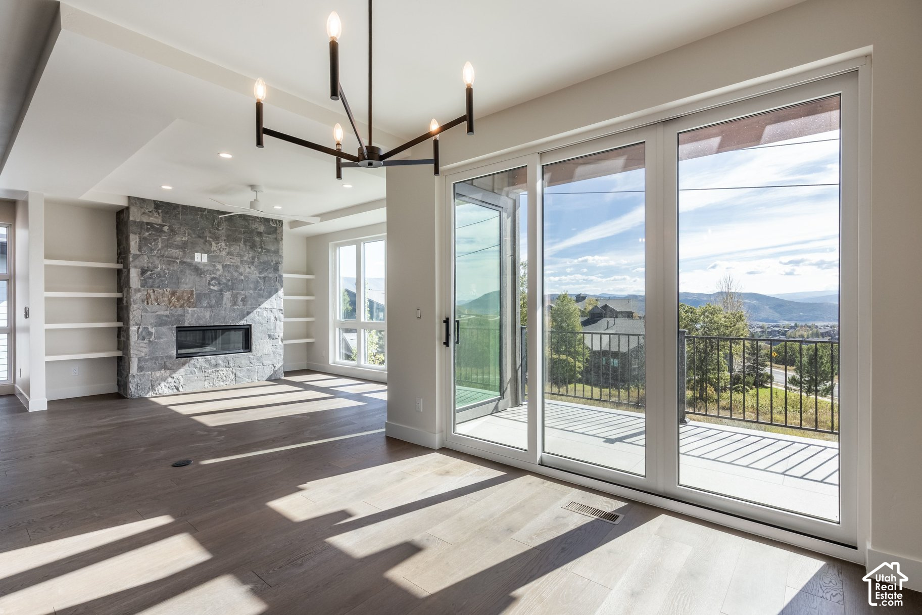 Vacant living room with stone fireplace and sliding doors opening to a mountain-view balcony