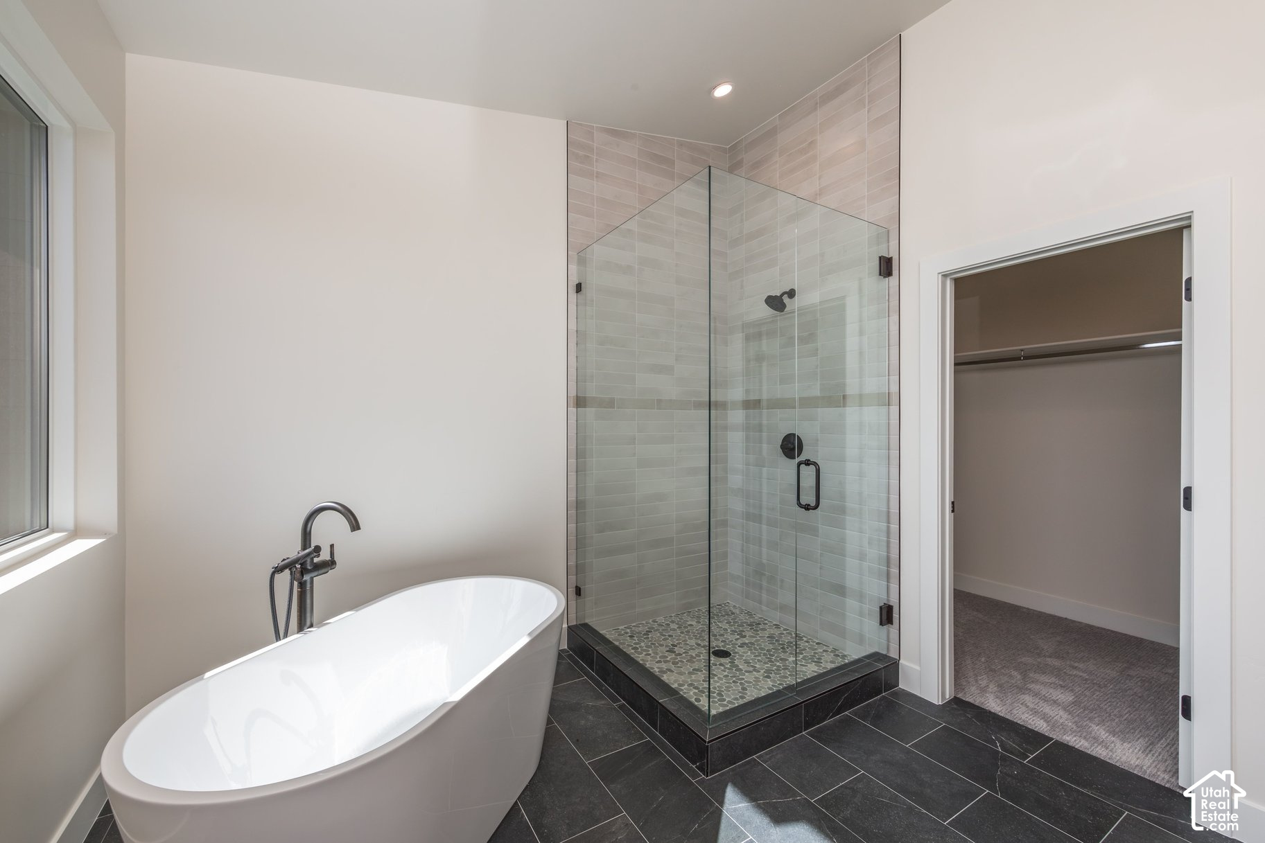 Modern bathroom with a freestanding soaking tub, glass shower, pebble floor, and dark tile flooring.