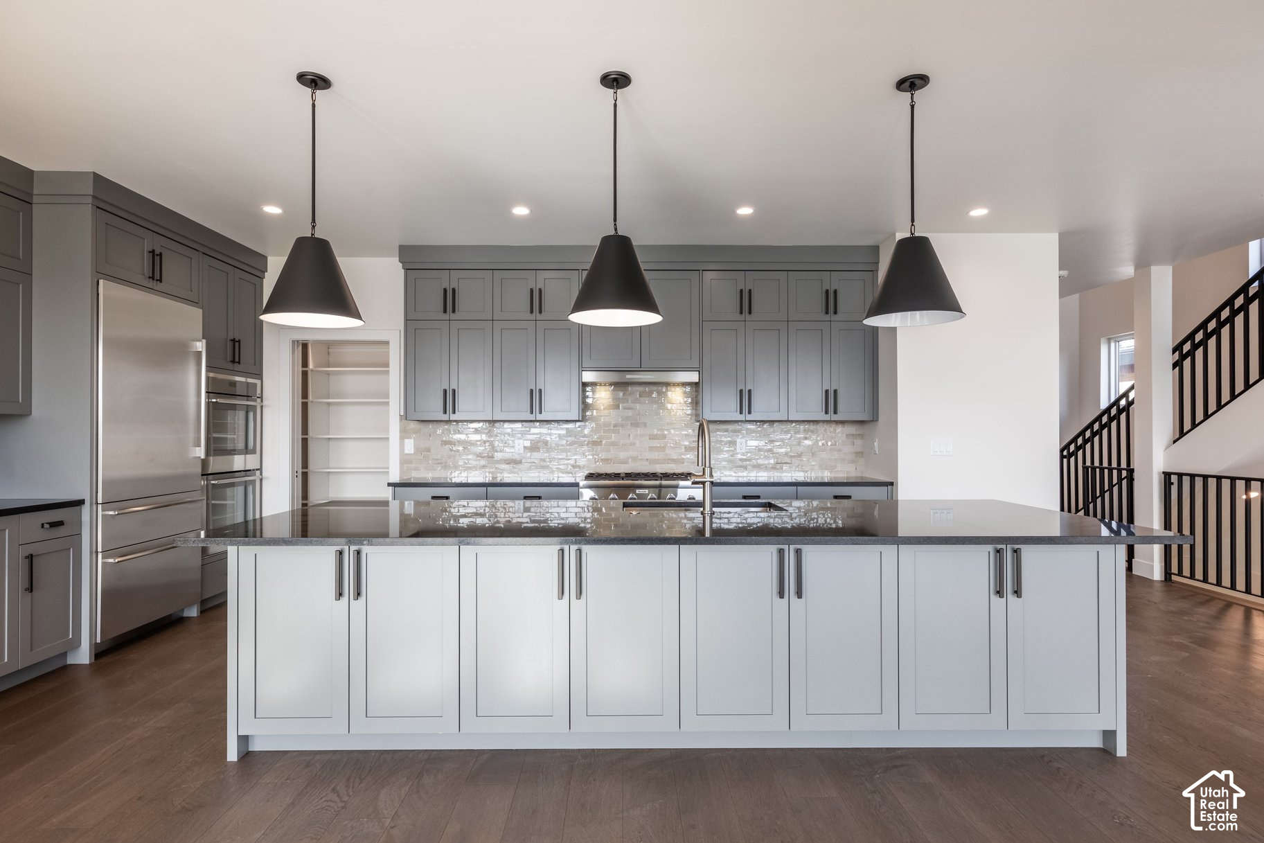 Modern kitchen with gray cabinets, stainless appliances, and a large island beneath three pendant lights.
