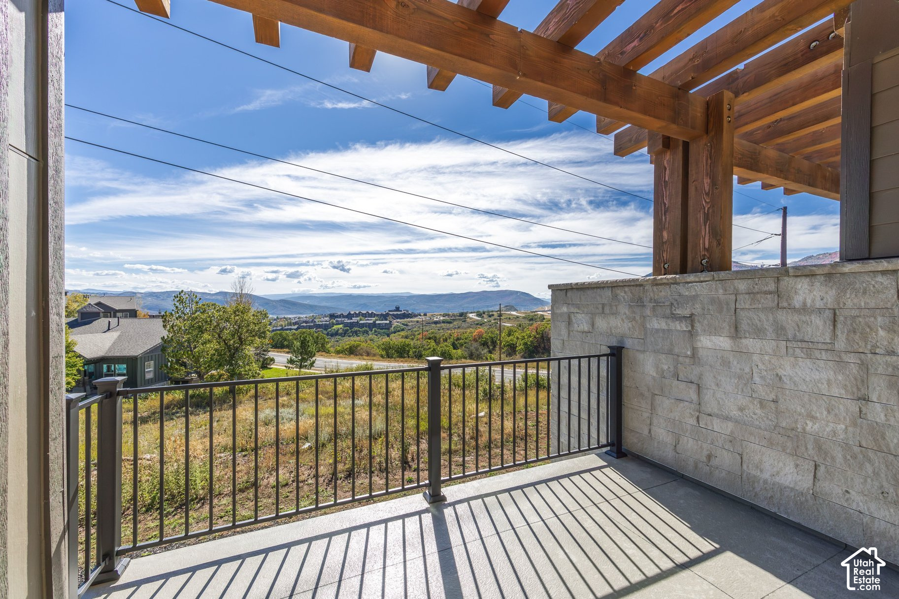 Balcony beneath a timber pergola overlooking autumn foliage, nearby homes, and mountain ridges.