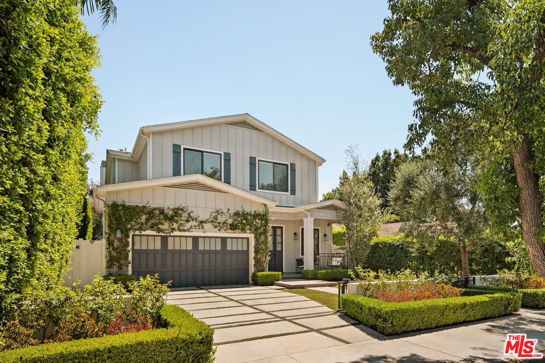 Two-story white house with a dark garage door, landscaped hedges, and a paved driveway.