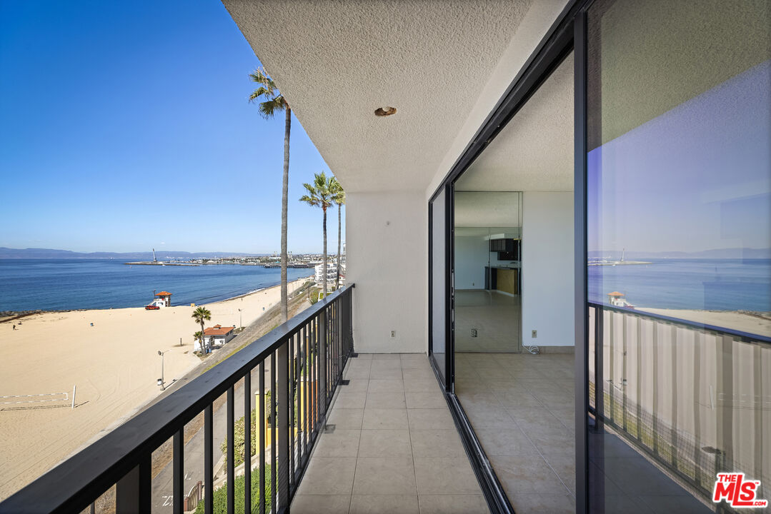 Beachfront apartment balcony with tiled flooring, glass doors, and ocean views.