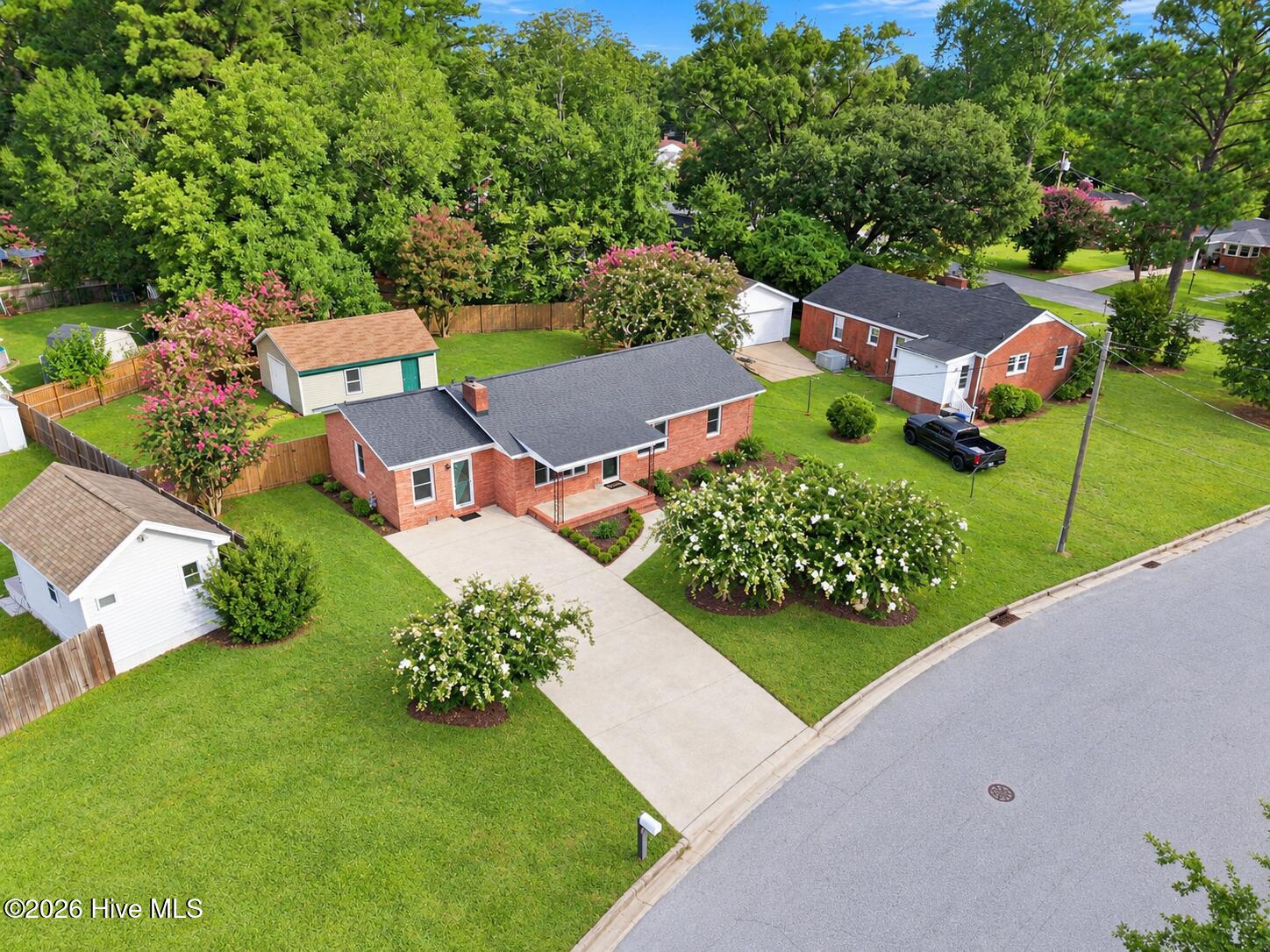 Brick ranch home with a broad lawn, driveway, and flowering trees, seen from above.