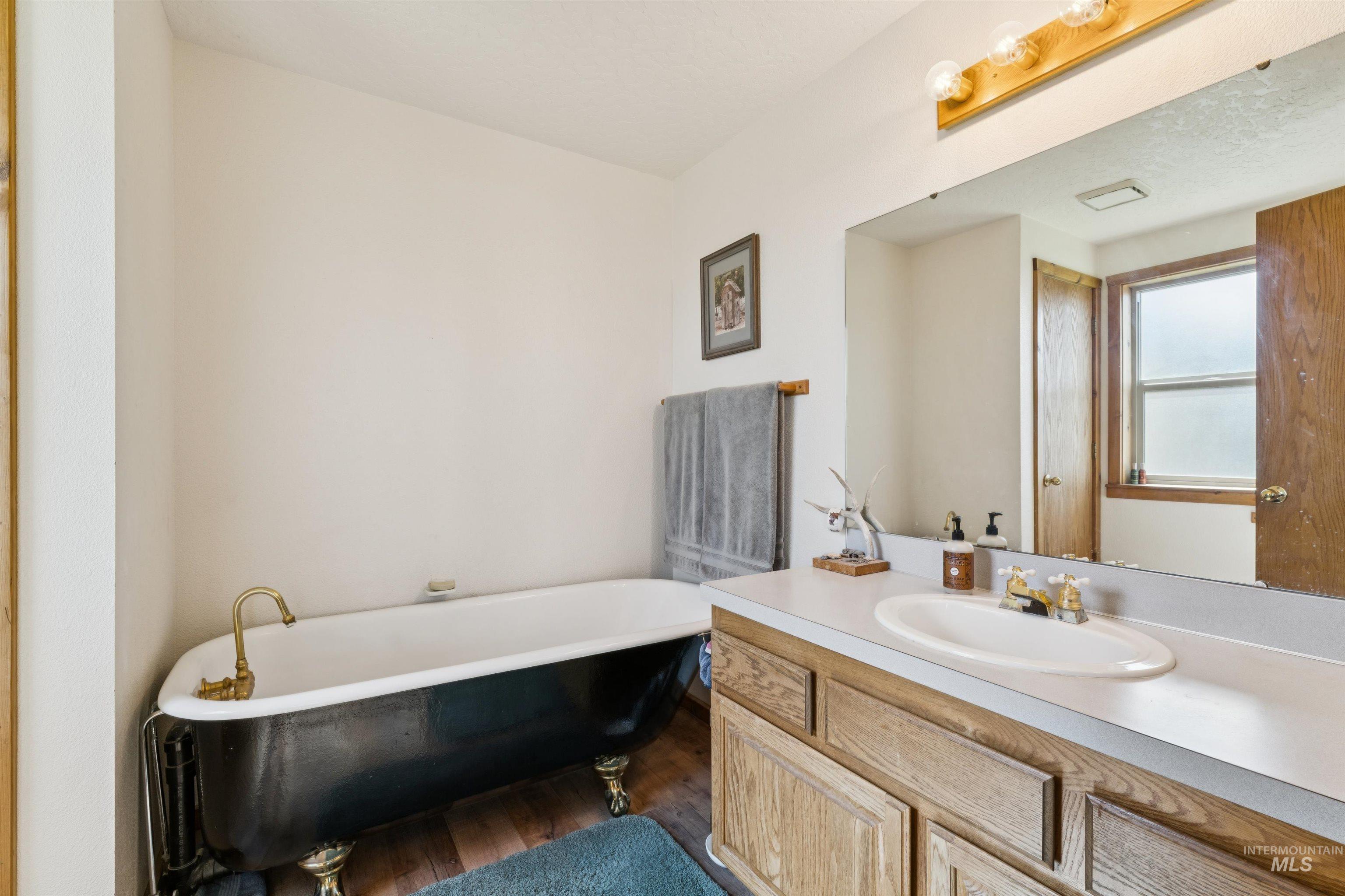 Bathroom with a black clawfoot tub, brass fixtures, and a wood vanity beneath a large mirror.
