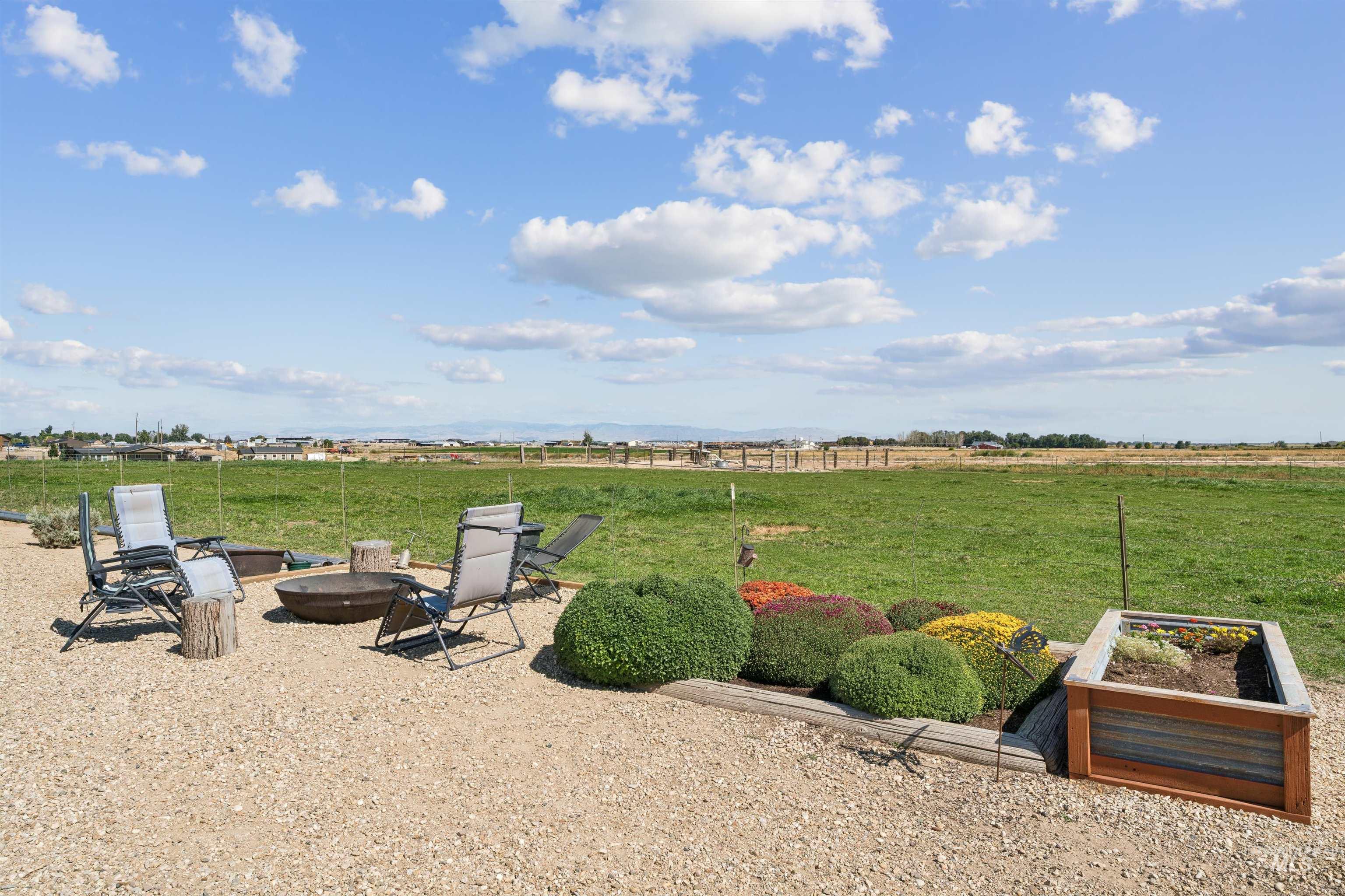 Backyard patio with lounge chairs, a fire pit, raised flower beds, and open fields beyond.