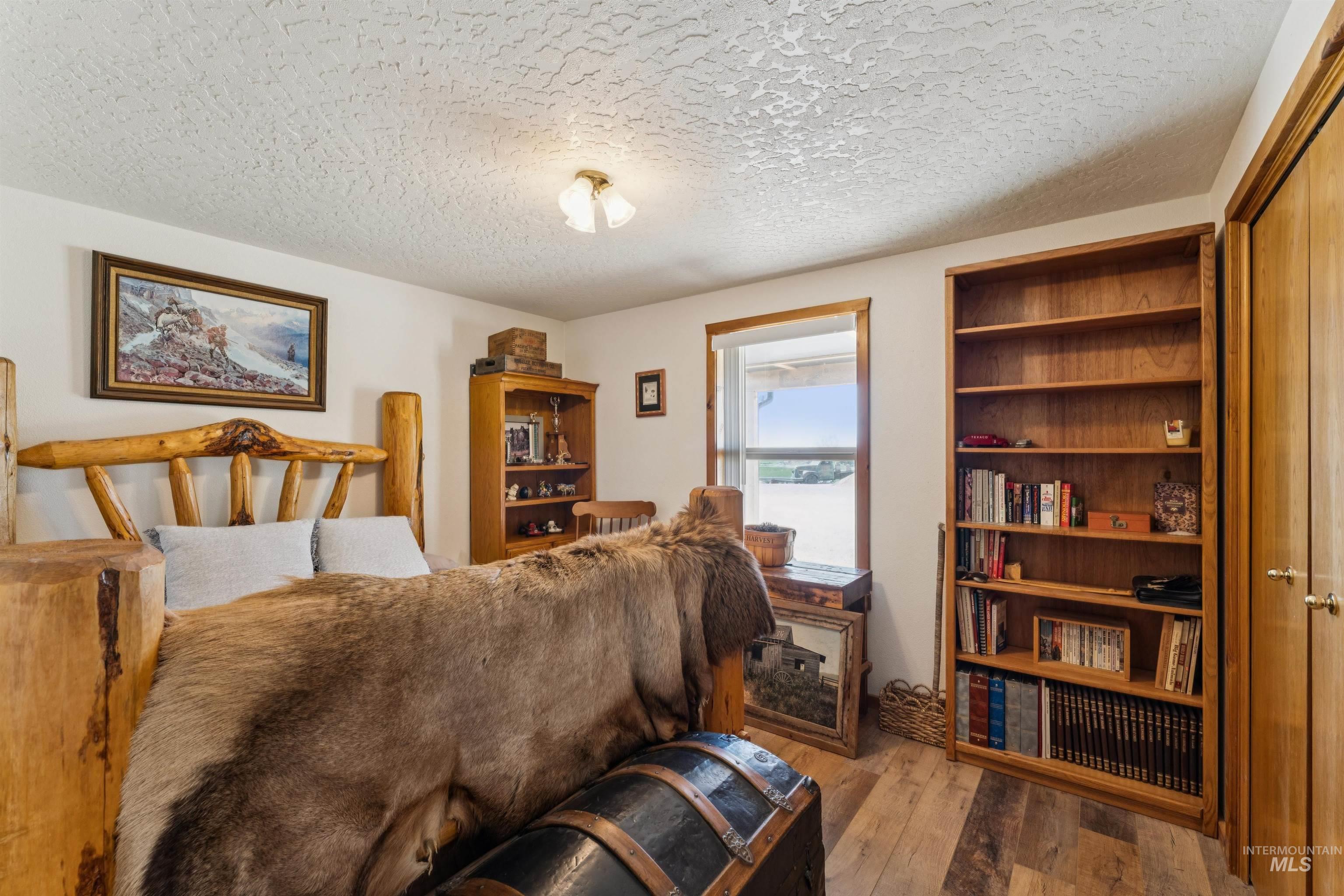 Rustic bedroom with a log bed, fur blanket, wood-plank floor, and built-in bookcase.